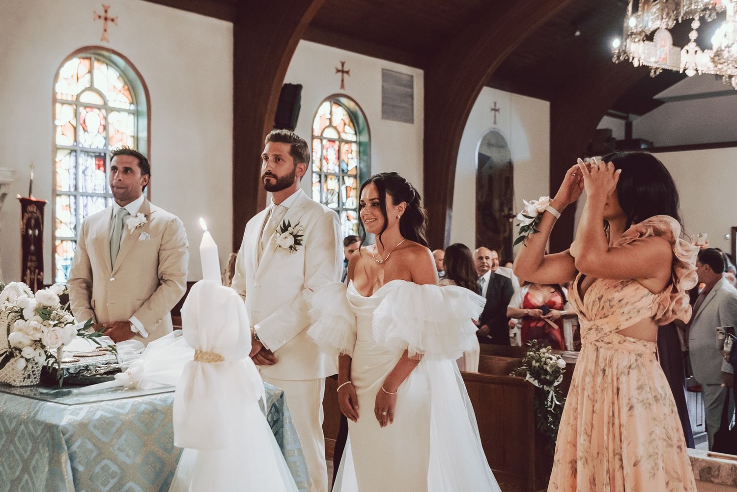 Bride and groom stand at the altar during a church wedding ceremony with emotional guests nearby.
