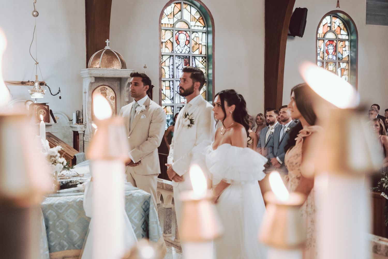 Bride and groom stand at the altar in a sunlit church with stained glass windows during a romantic wedding ceremony.