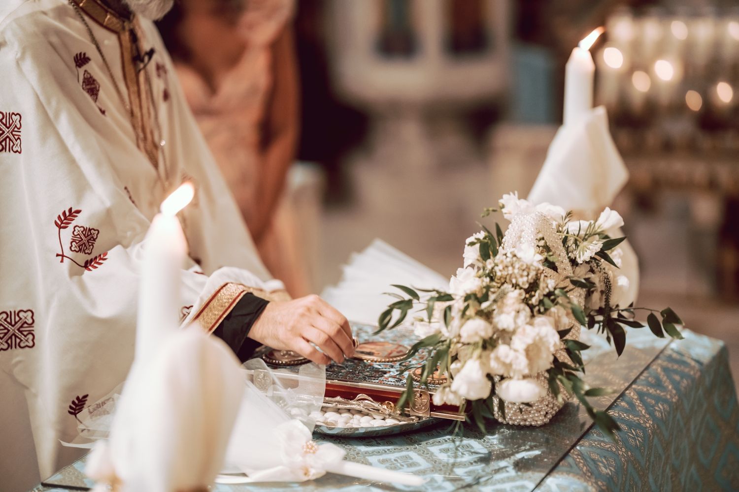 Bride in embroidered dress signing wedding documents at decorated altar with white flowers and candles.