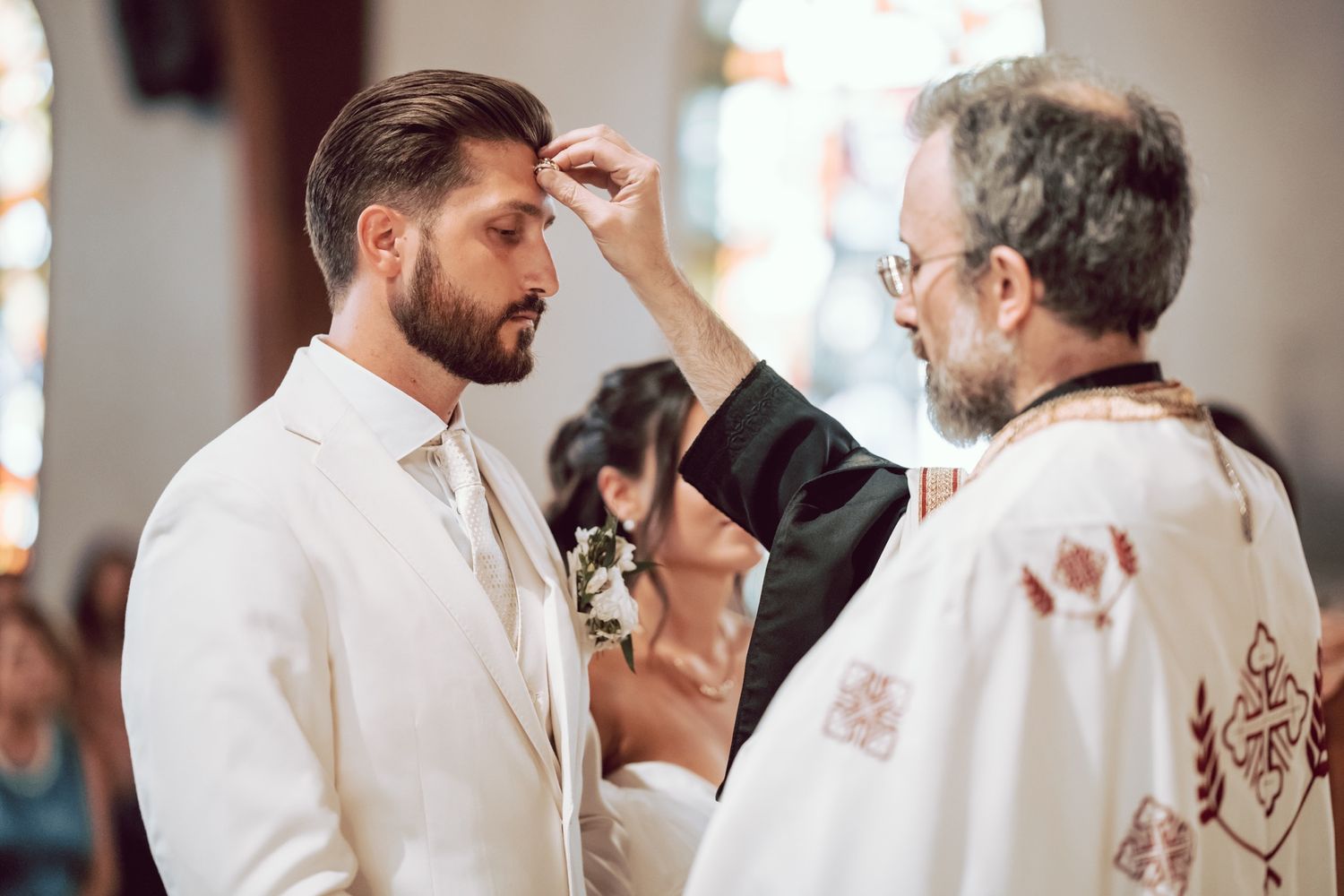 Priest anointing groom with oil during Orthodox wedding ceremony in church.