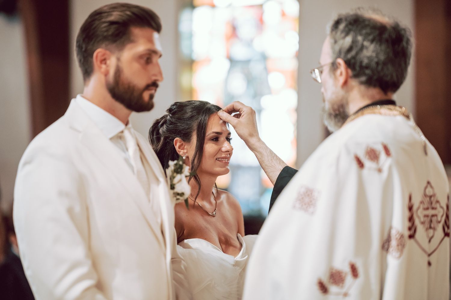 Orthodox priest blessing bride during wedding ceremony while groom watches in church.