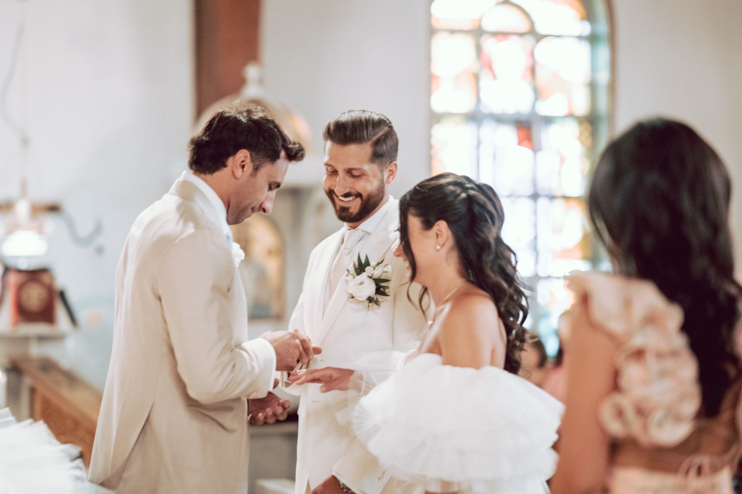 Groom exchanges rings with bride as smiling officiant witnesses the wedding ceremony indoors.