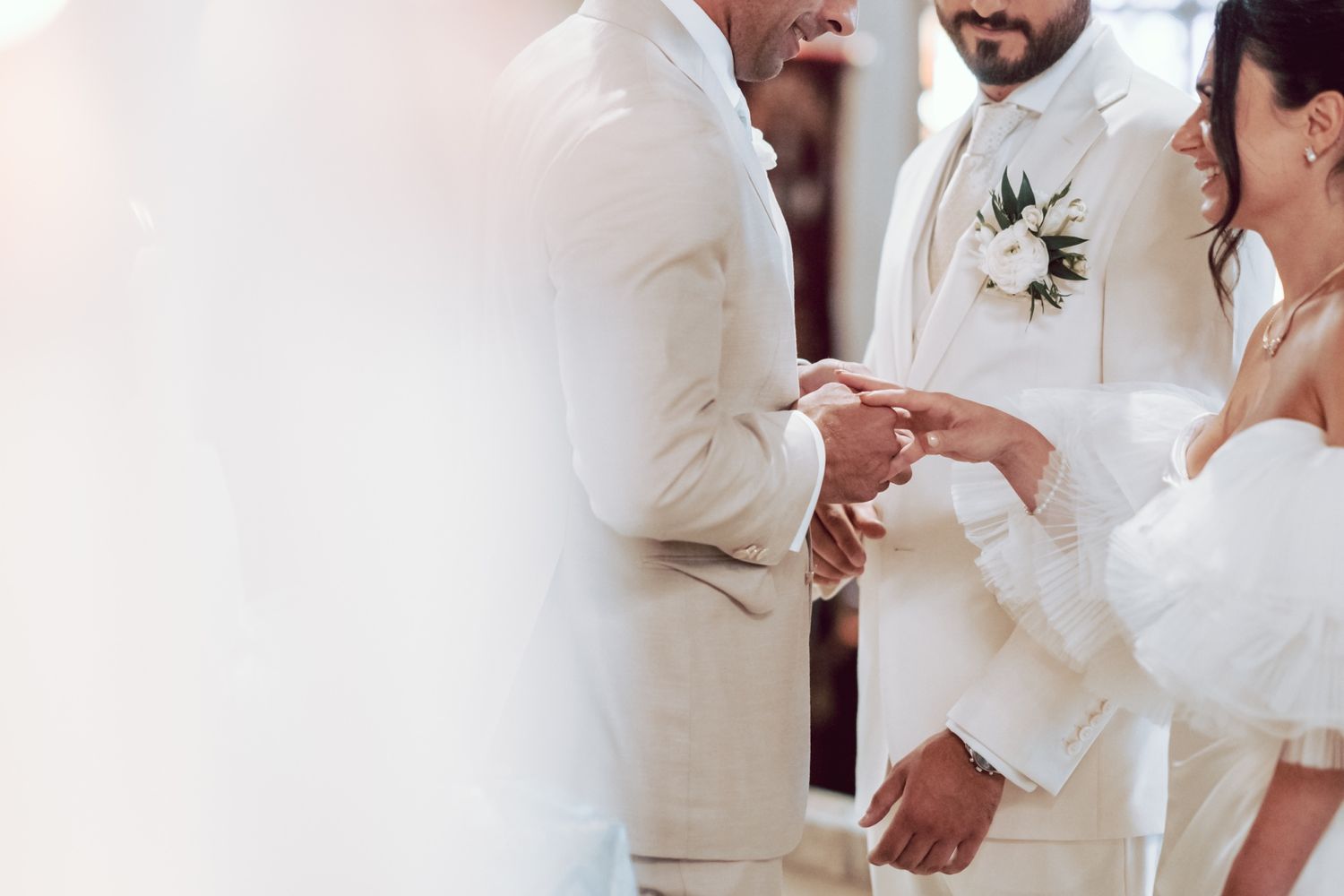 Two grooms in white suits exchange wedding rings during an elegant outdoor ceremony.