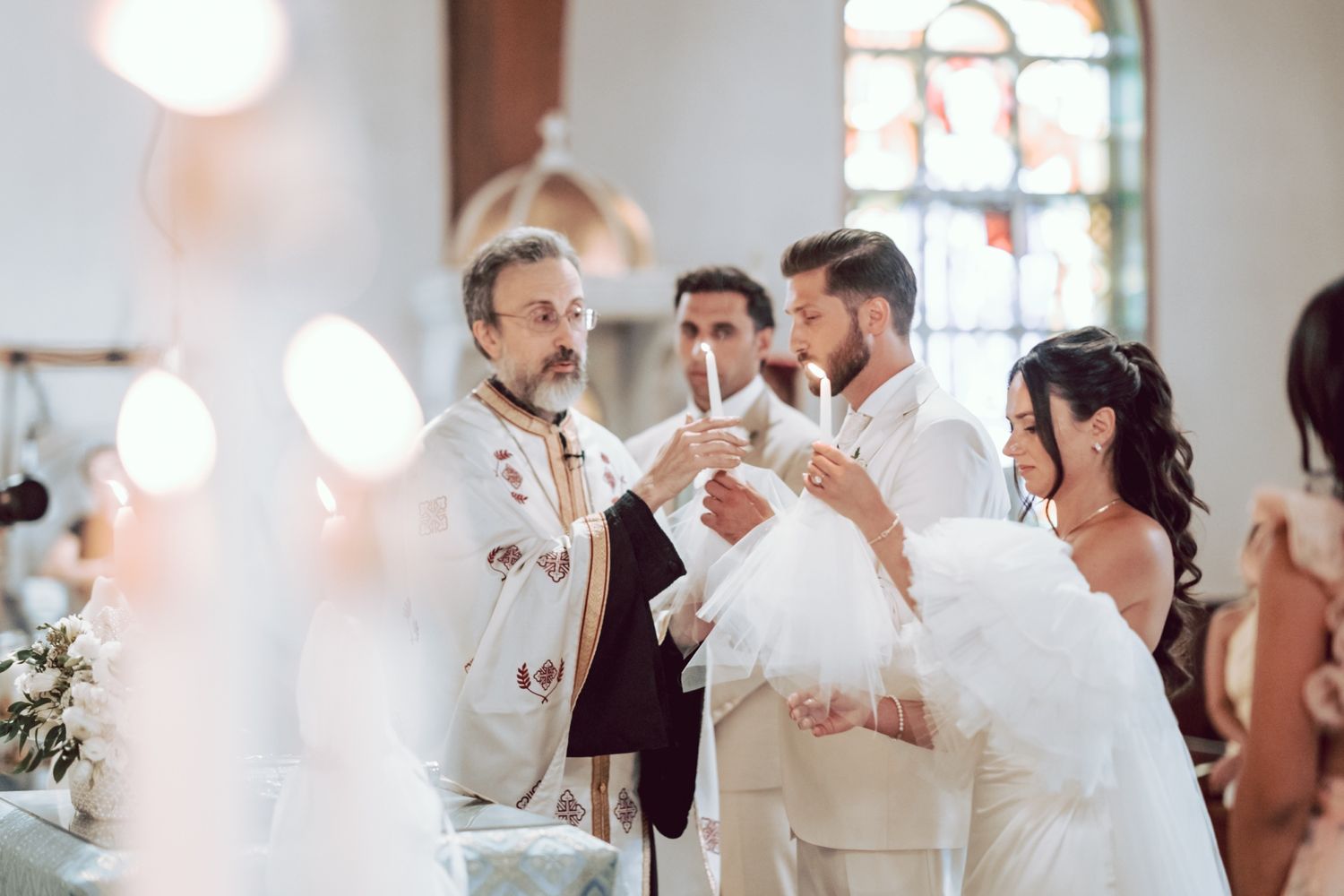 Orthodox priest leads wedding ceremony with bride and groom holding candles at the altar.