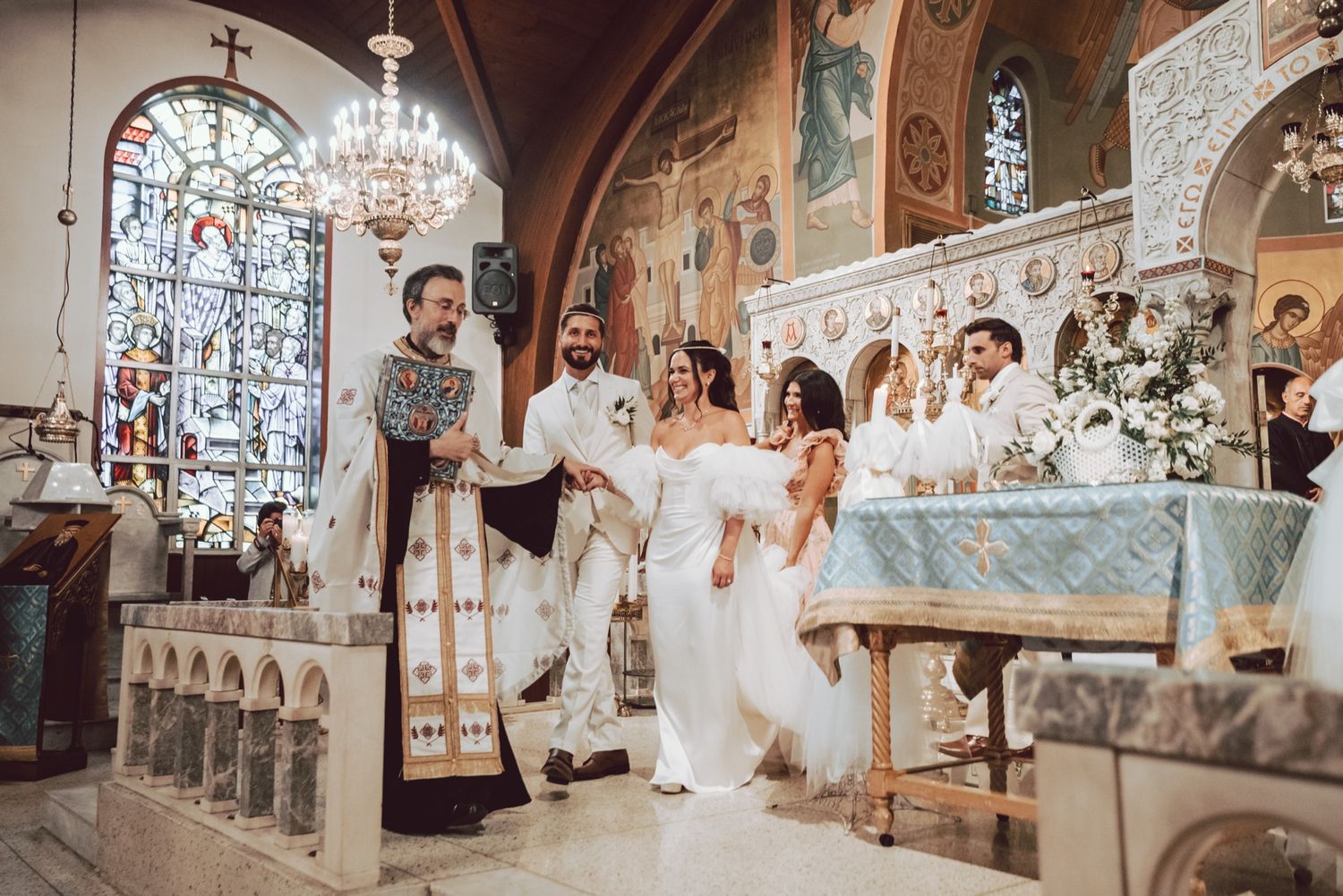 Orthodox priest guides bride and groom during traditional church wedding ceremony at decorated altar.
