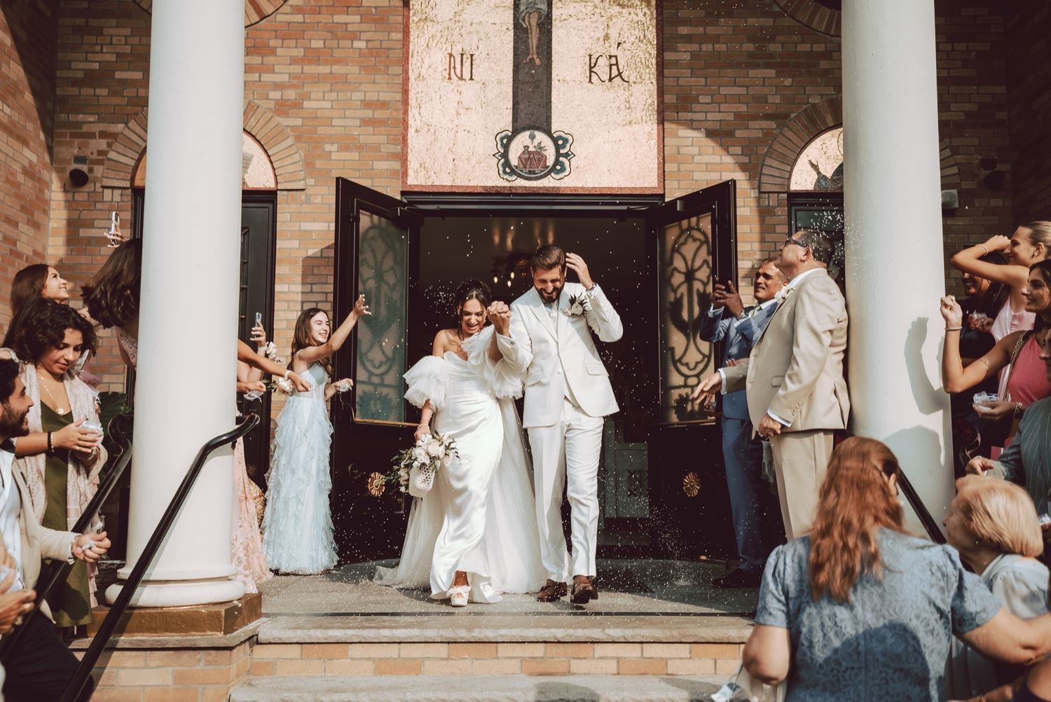 Newlyweds exit through grand church doors as guests celebrate with confetti on the steps outside.