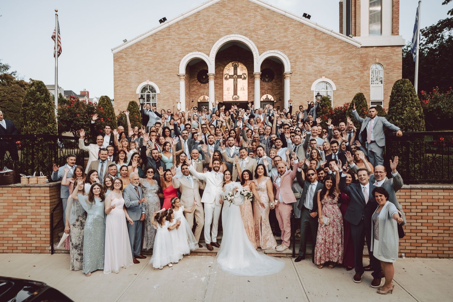 Large wedding party group photo on church steps with bride and groom surrounded by guests.