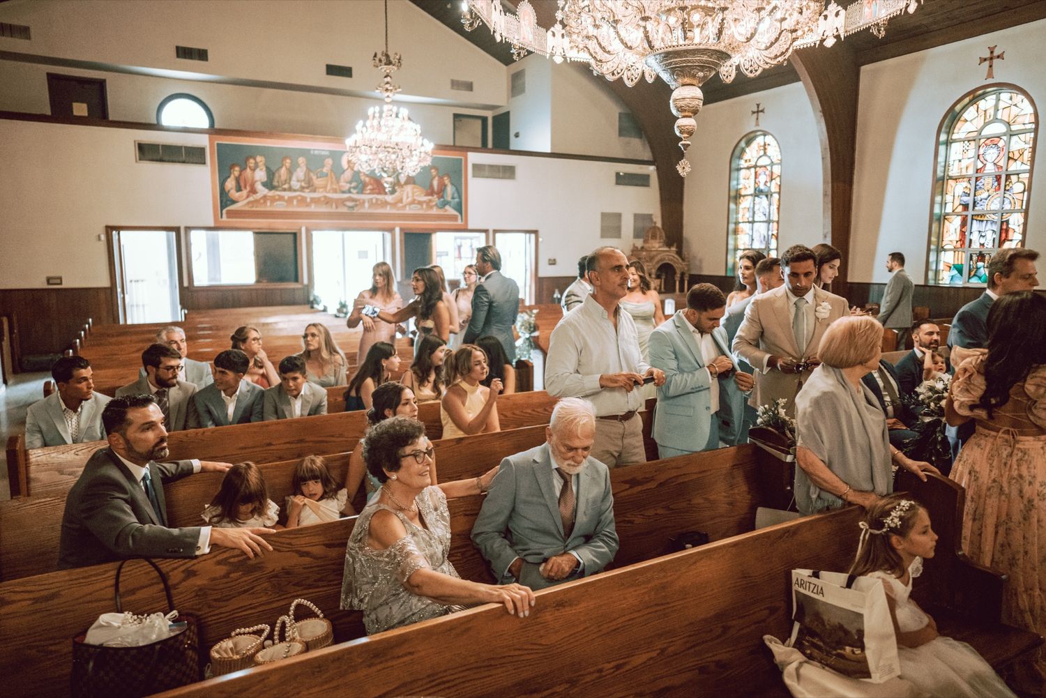 Guests gather in a historic church with wooden pews and stained glass windows during a wedding ceremony.