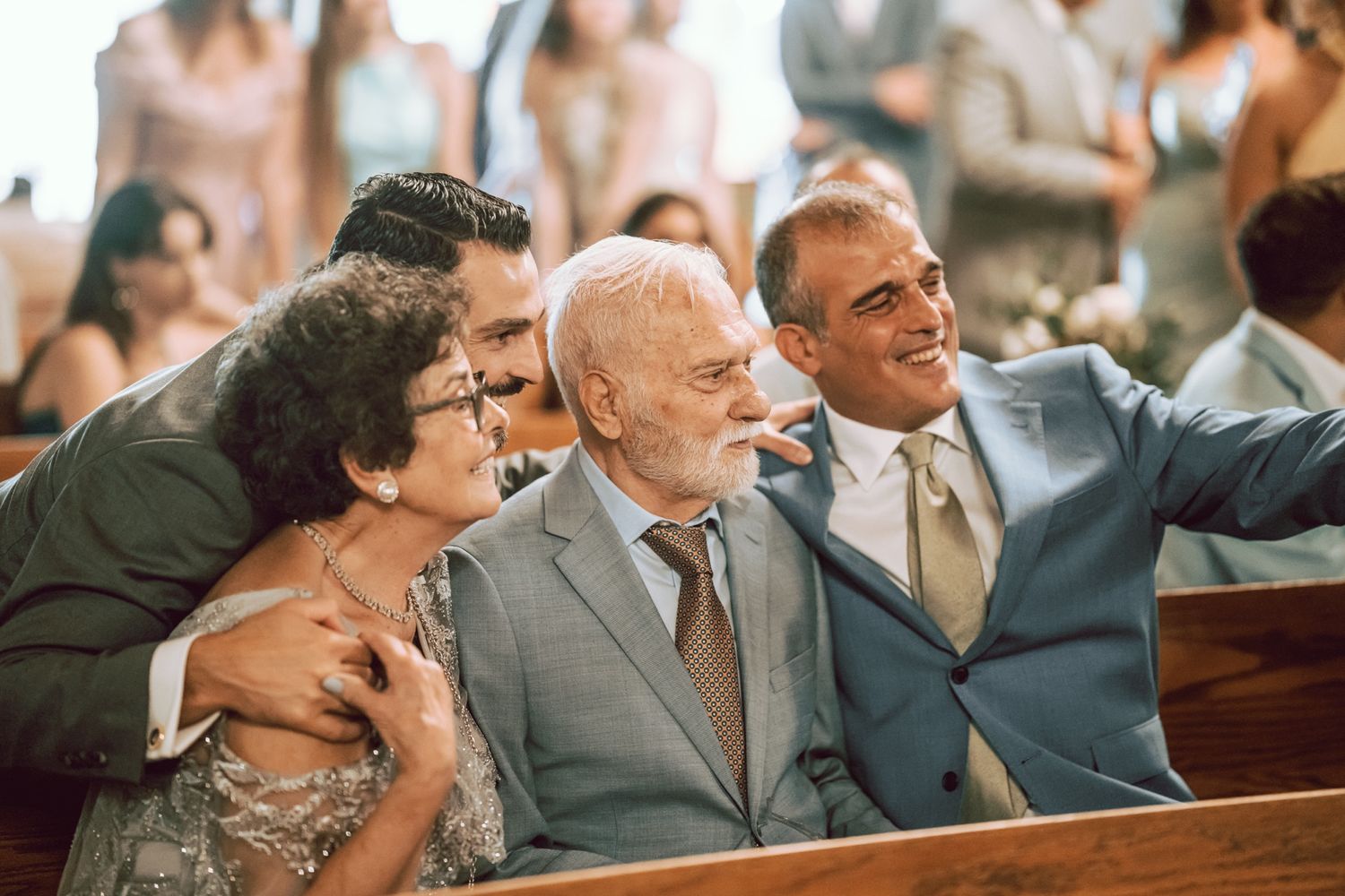 Family members smile and take a selfie together in church pews during a wedding ceremony.