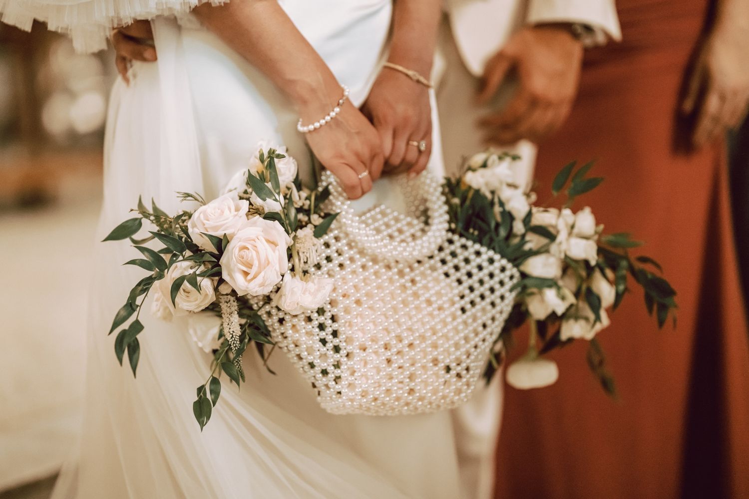 Bride holding a woven pearl handbag filled with white roses and greenery at a wedding.