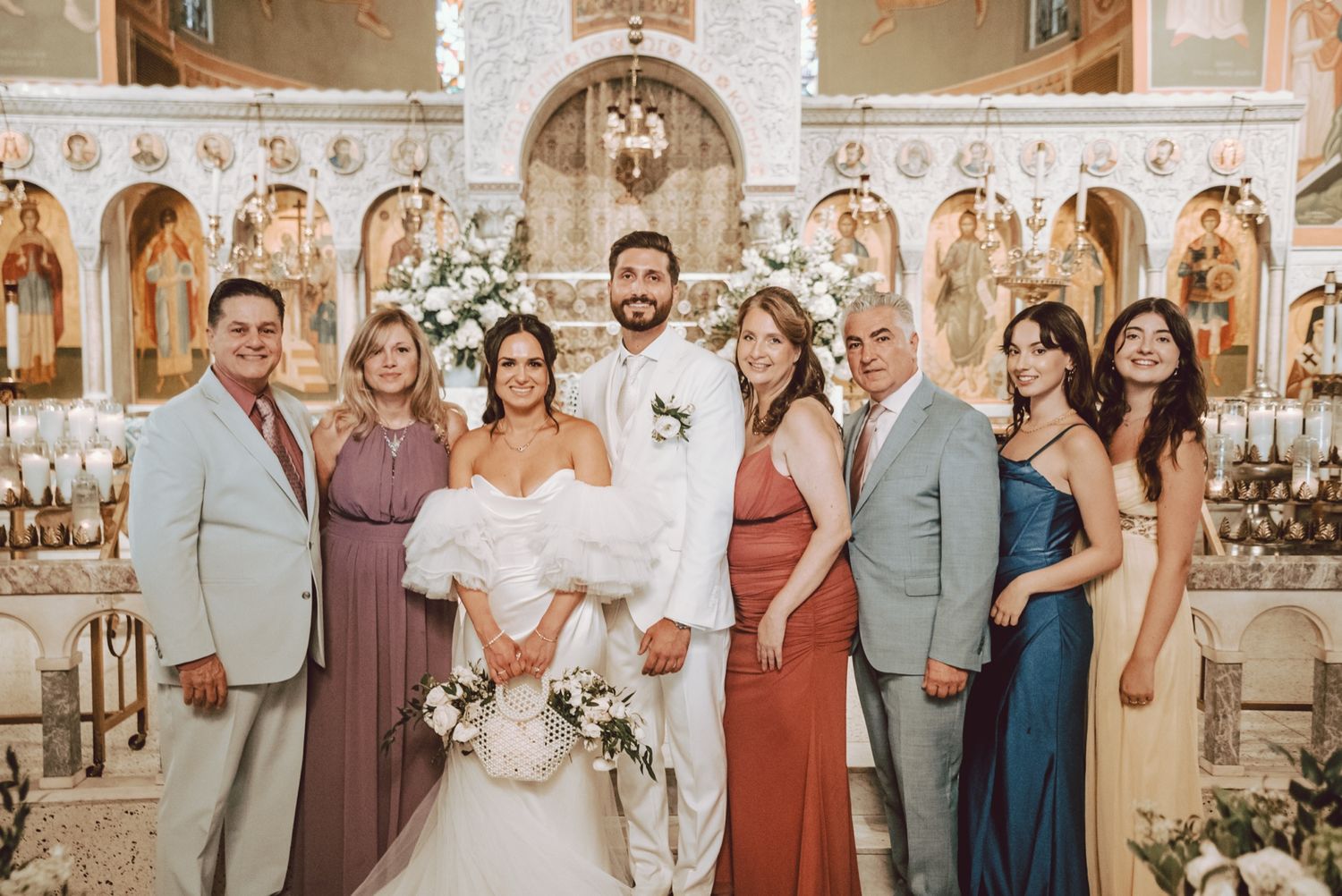 Wedding party family portrait inside an ornate Orthodox church, bride and groom centered with six formally dressed relatives.