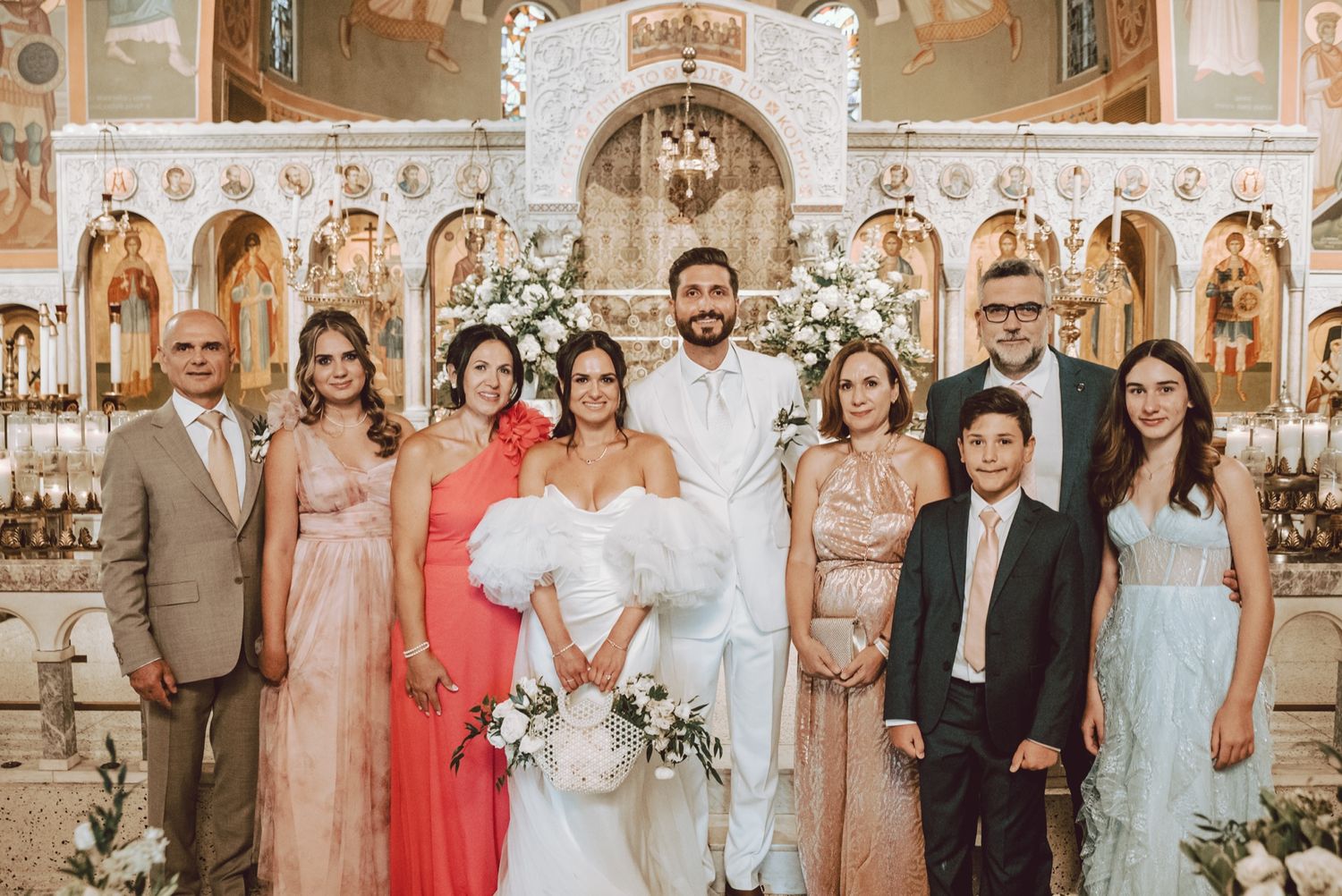 Wedding party poses together in an ornate church, featuring the bride and groom surrounded by family in formal attire.