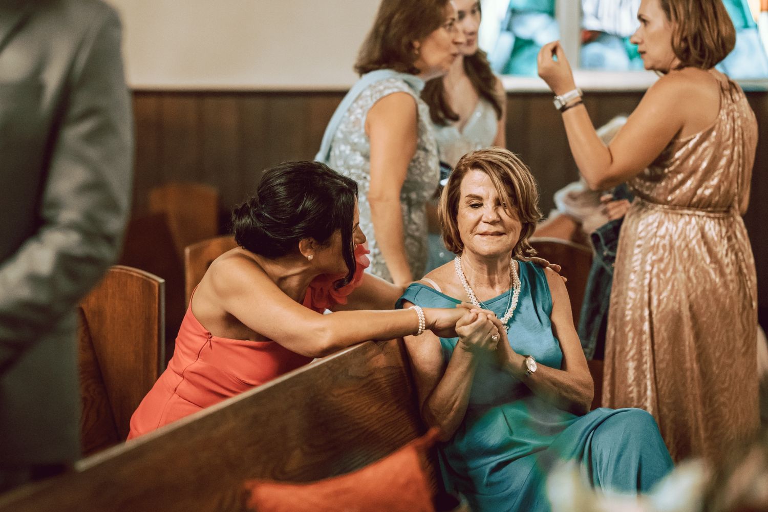 Women in elegant dresses socializing at a wedding reception inside a church with wooden pews.