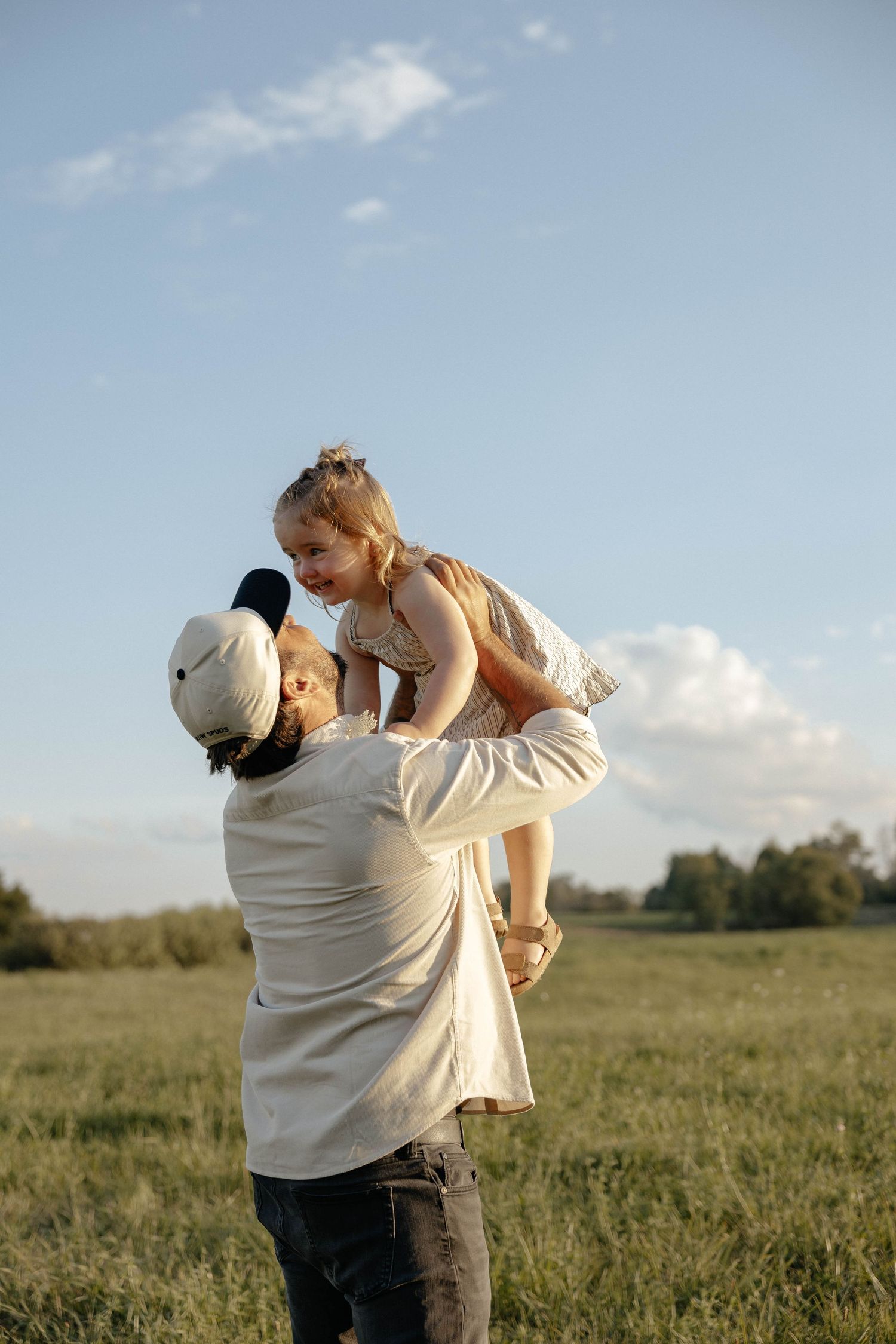 A mother twirls her young daughter in a sunny green meadow, both wearing matching striped dresses.