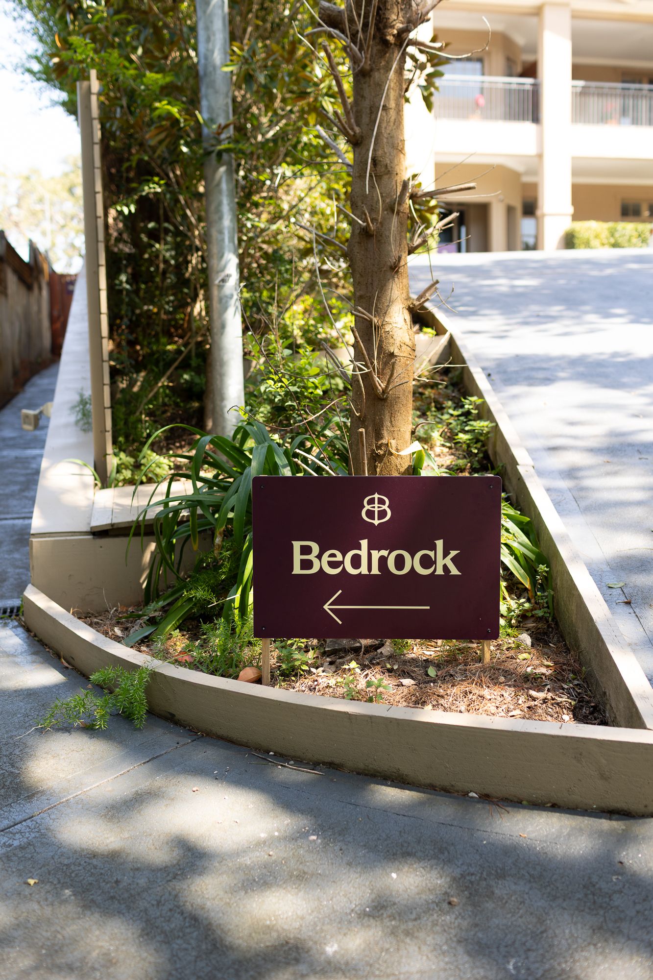Bedrock venue sign with arrow pointing left, set in a garden bed surrounded by tropical plants and trees.