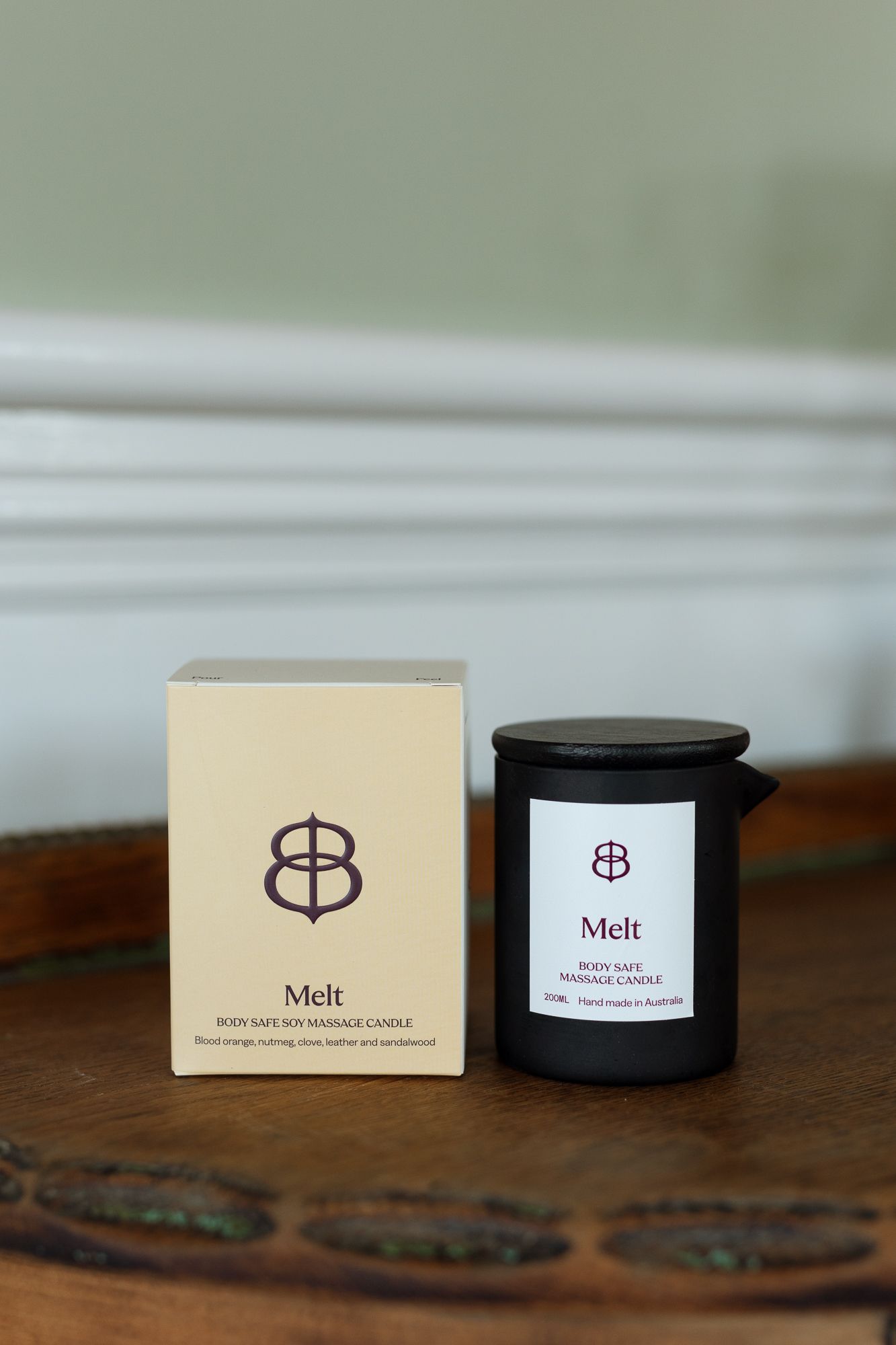 Melt body safe soy massage candle in black jar with cream gift box on wooden surface.