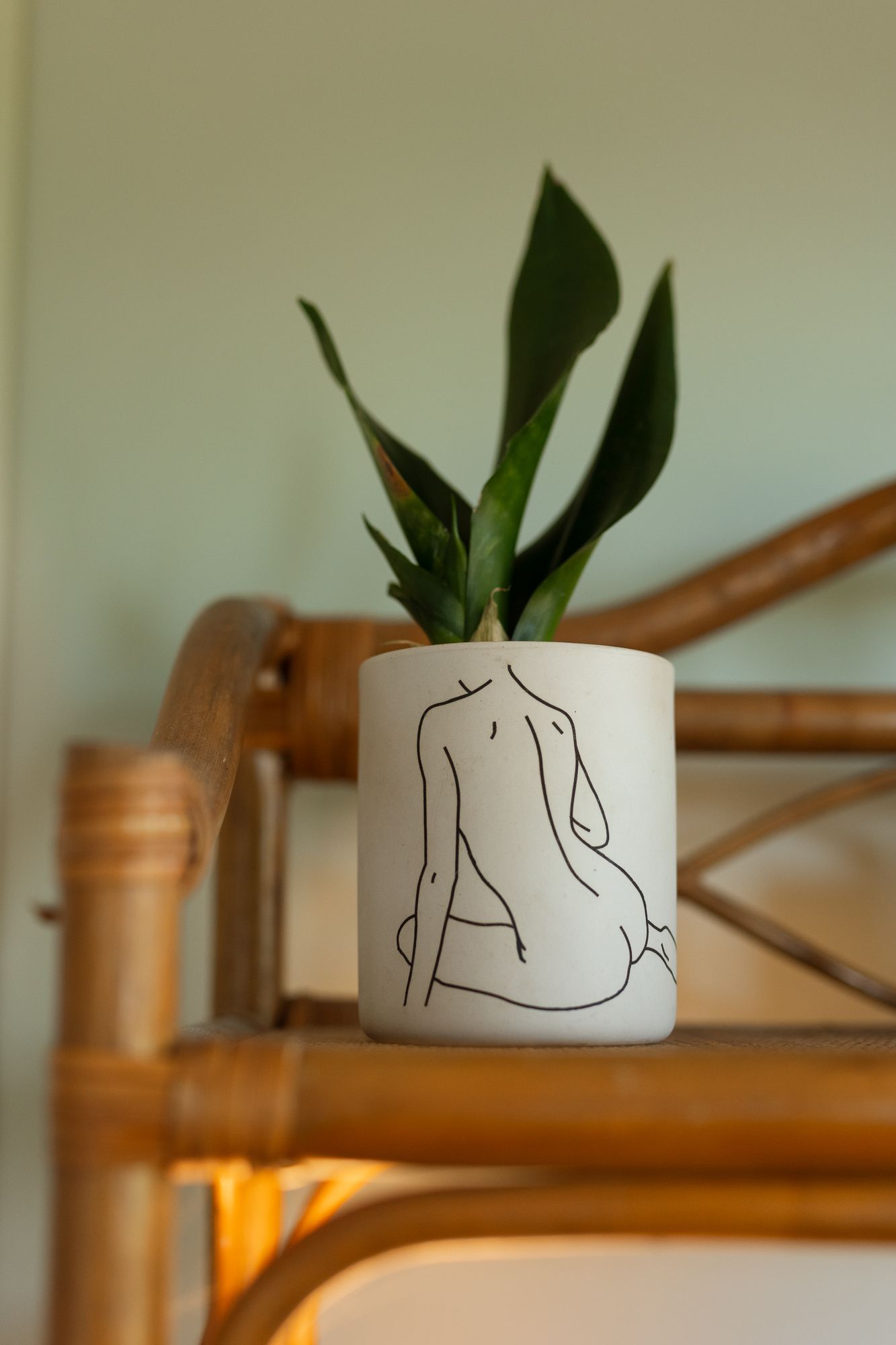 White ceramic planter with female line art holding a green plant on a rattan shelf.