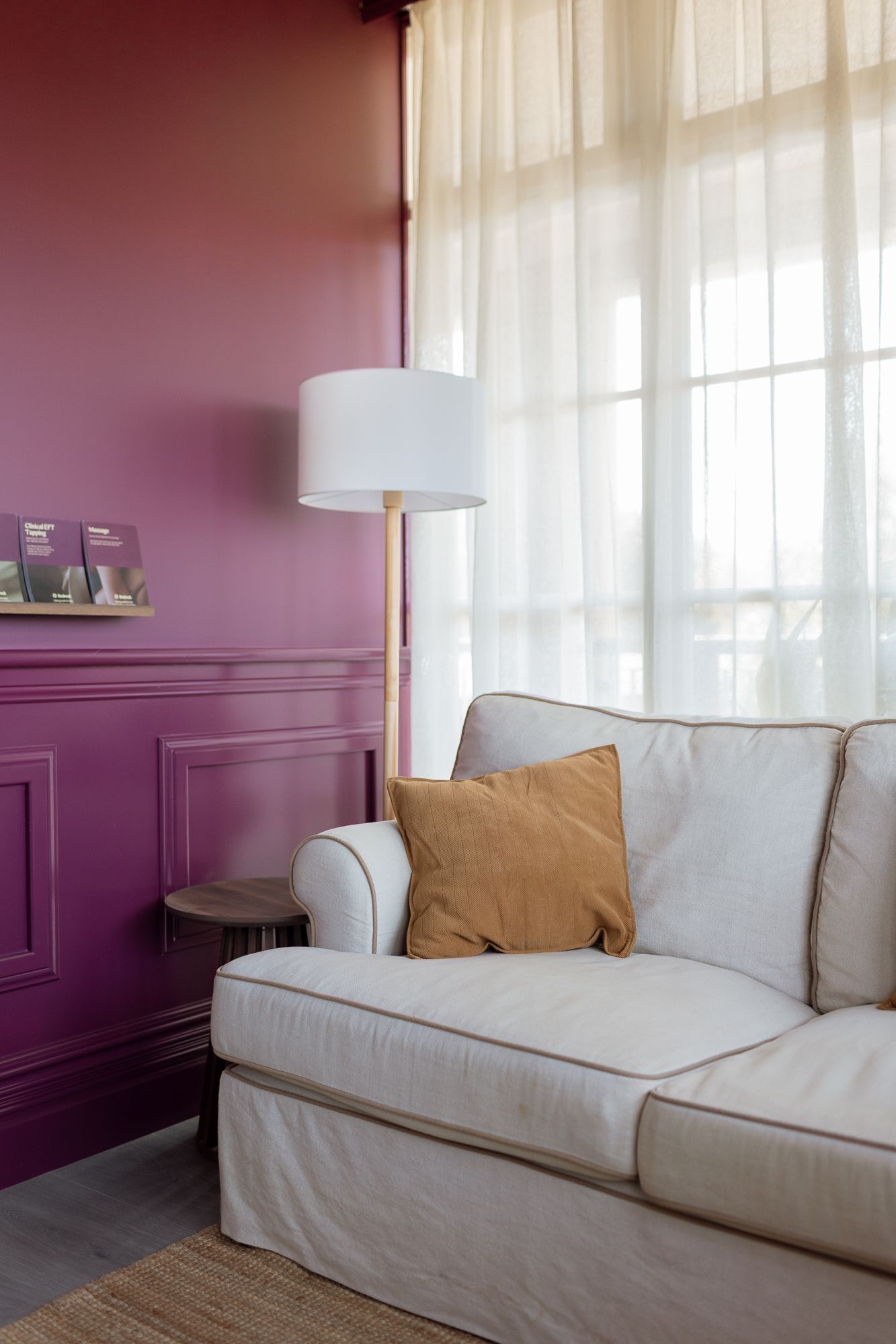 Cozy living room corner with a white sofa, mustard pillow, gold floor lamp, and elegant purple wainscoting wall.