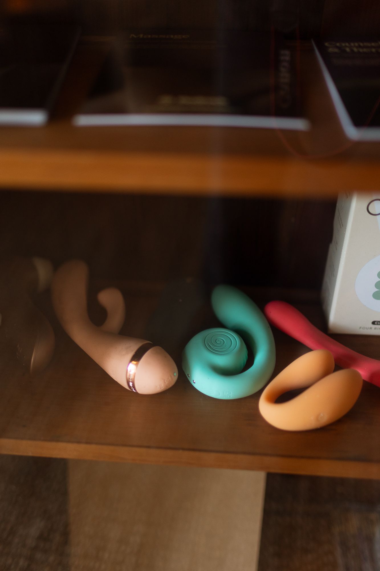 Collection of colorful adult pleasure toys displayed on a wooden shelf behind glass.