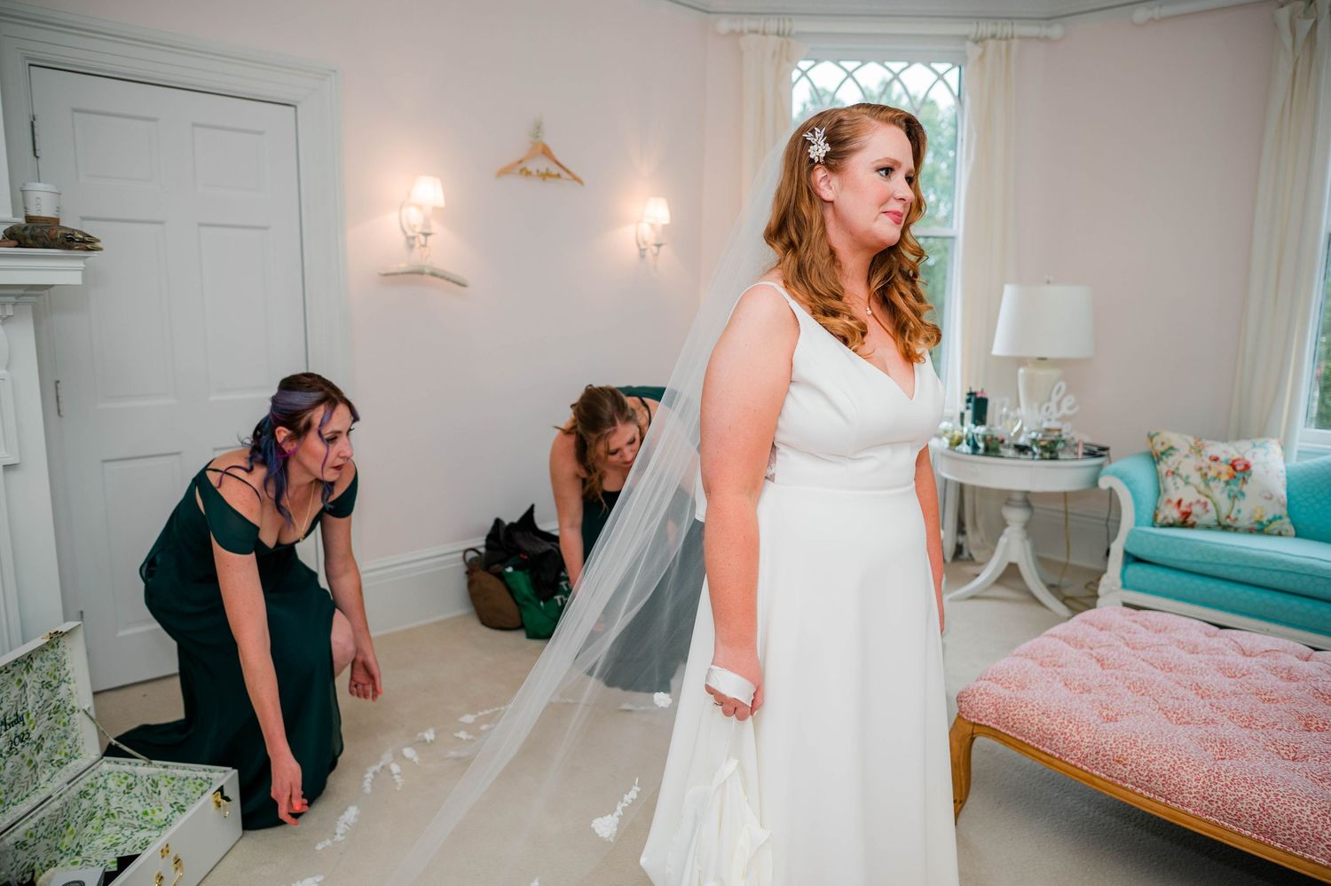 Bride in white gown with veil being adjusted by bridesmaids in an elegant room before wedding ceremony at Lounsbury House, Ridgefield, CT