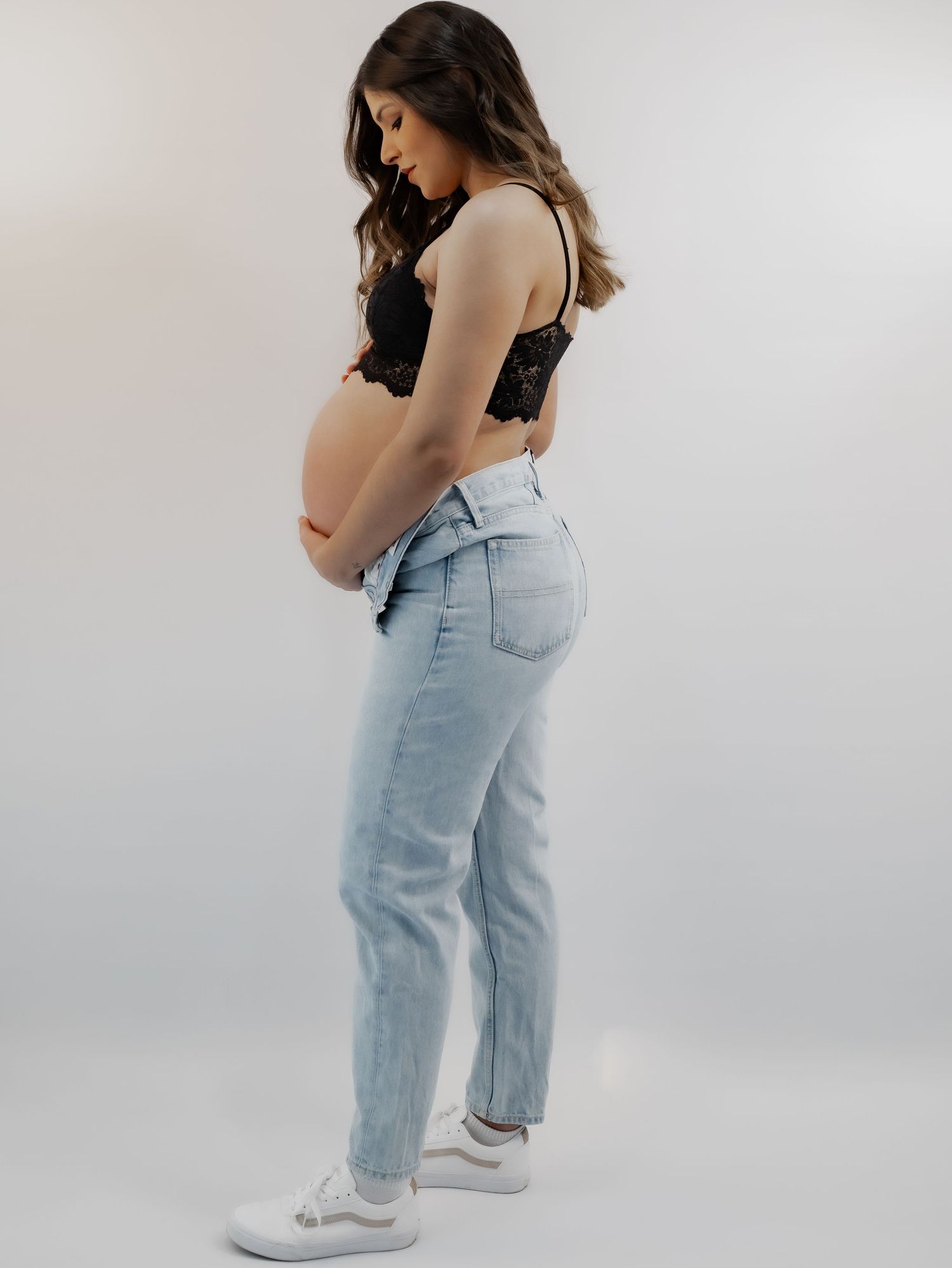 A smiling couple cradles a pregnant belly during a maternity photo shoot against a white background.