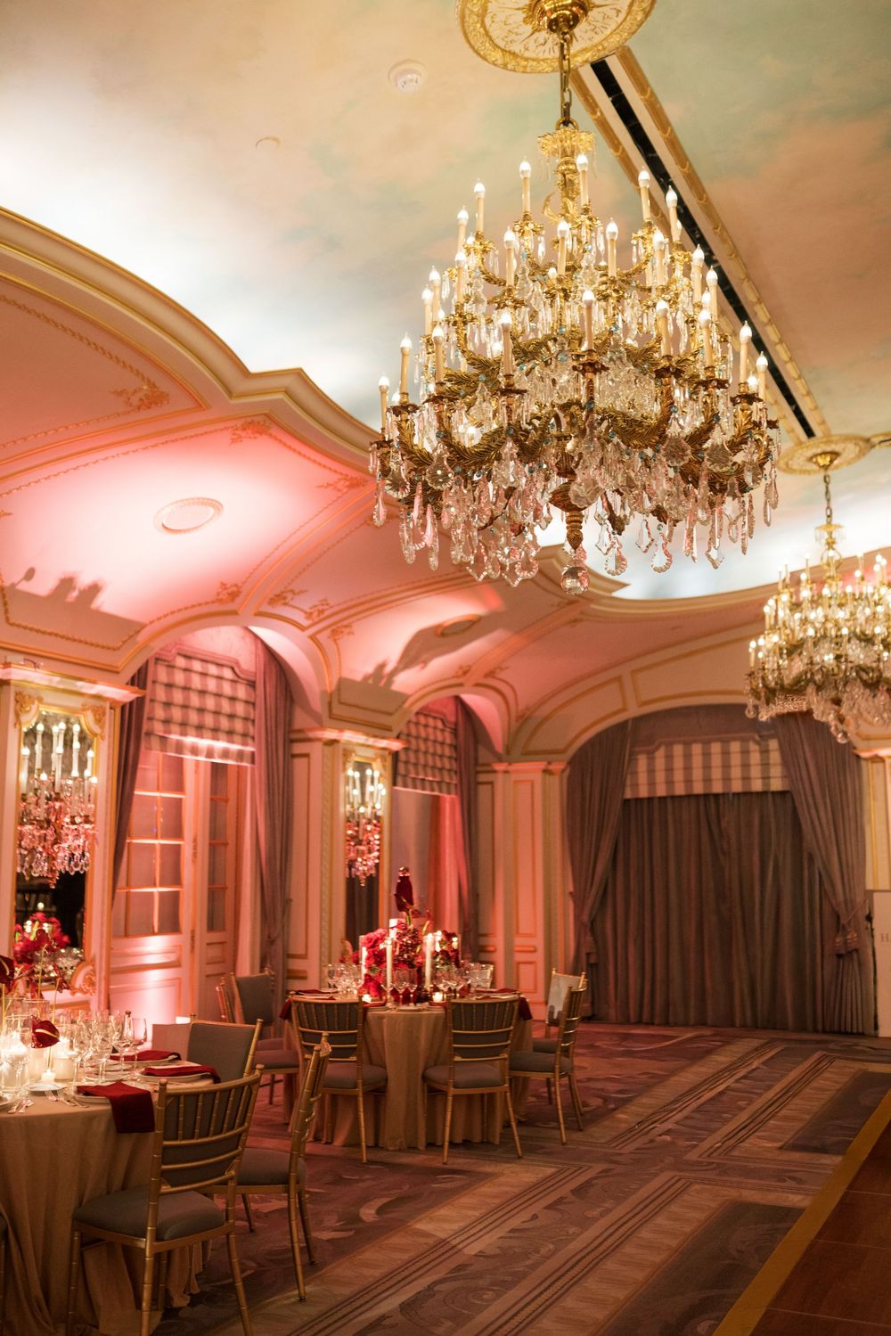 Elegant ballroom with crystal chandeliers, gold chairs, and pink uplighting for a luxurious event setting.