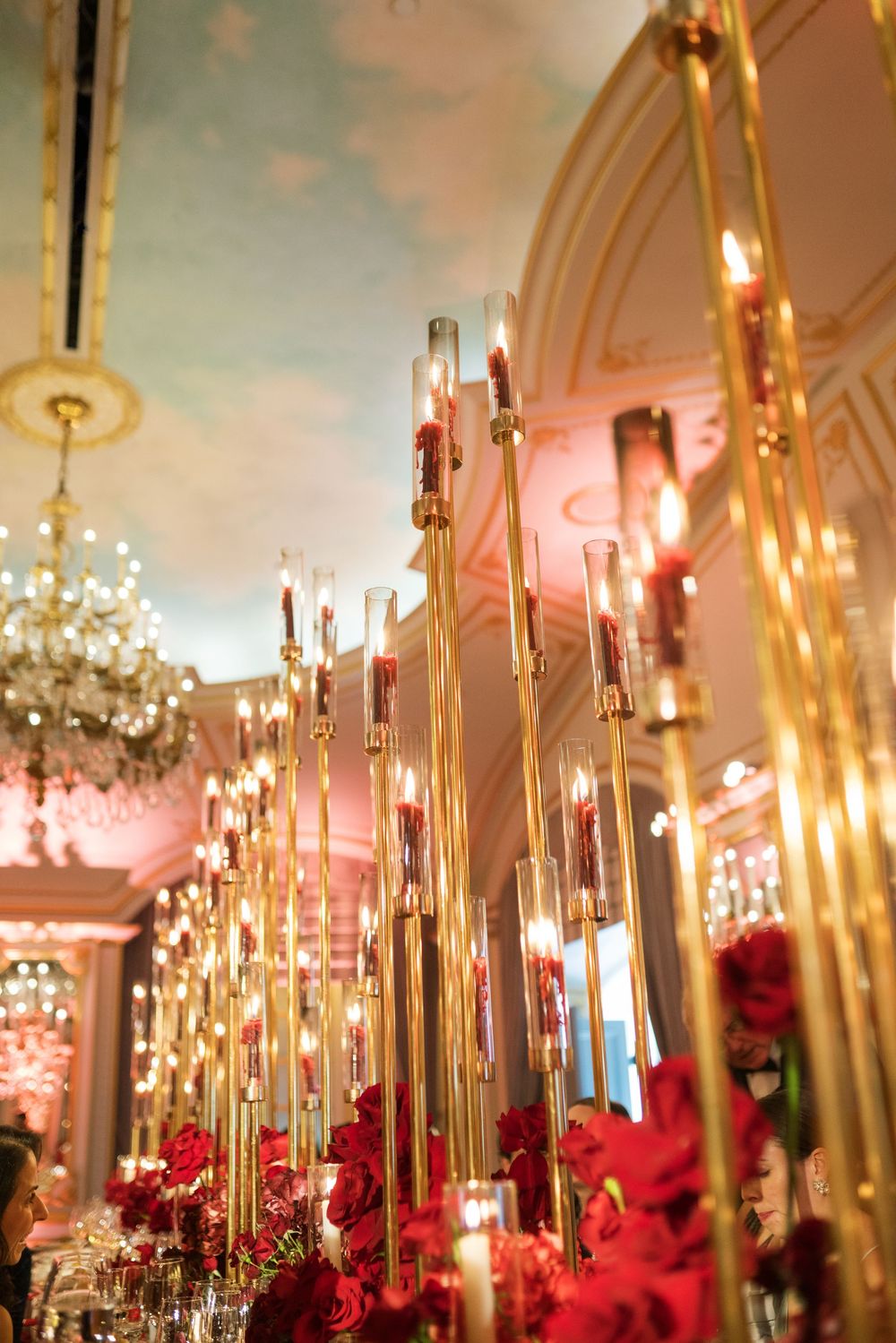 Elegant gold candelabras with red roses and glowing candles in a grand ballroom with chandelier.