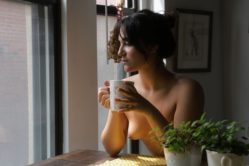 Woman standing nude against deep red curtains, turned slightly to the side in a quiet portrait