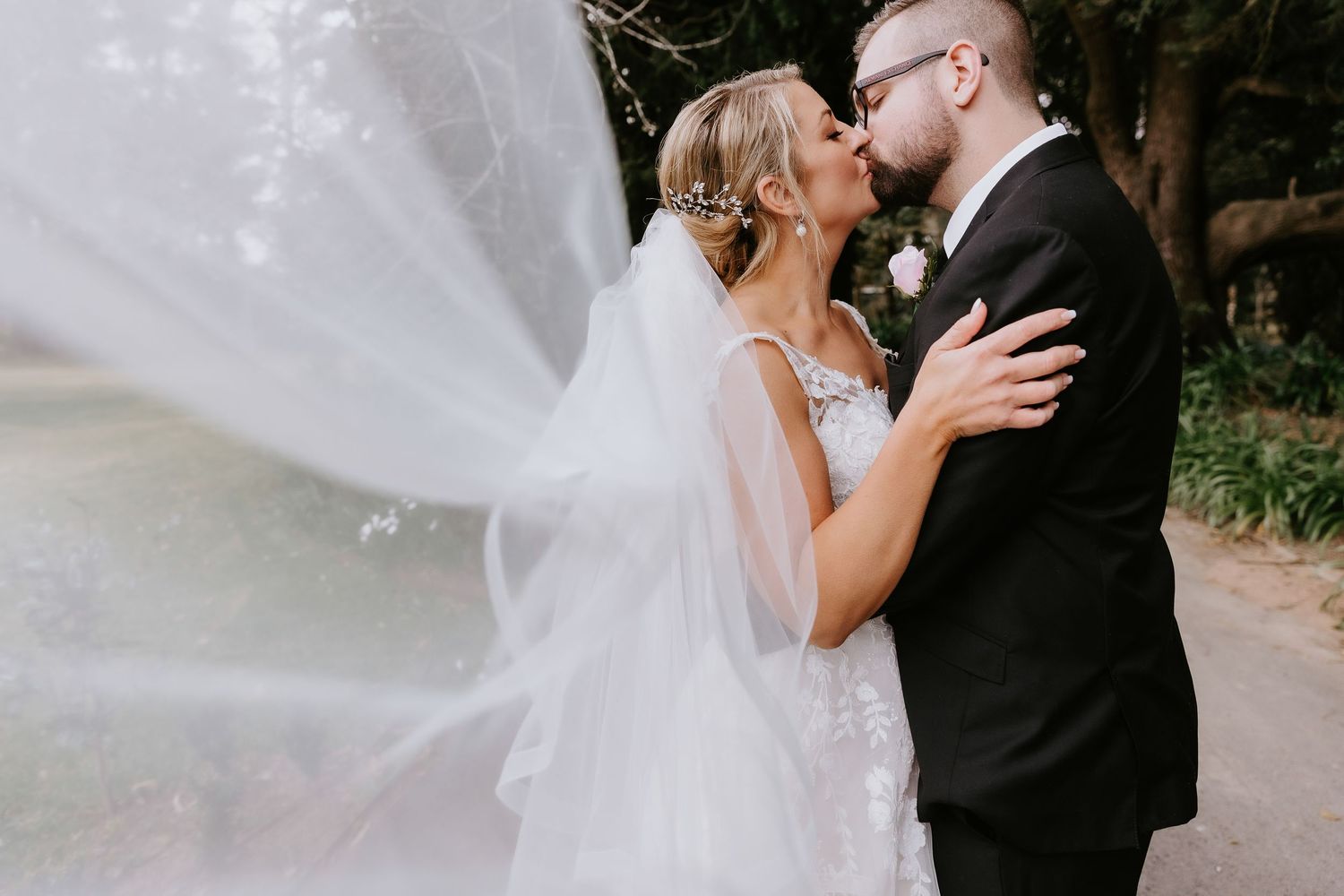 Elegant wedding couple portraits with flowing white veil in dreamy outdoor setting.