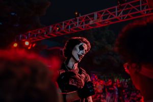 Person in dramatic clown face paint costume at a dark outdoor Halloween event with red lighting.