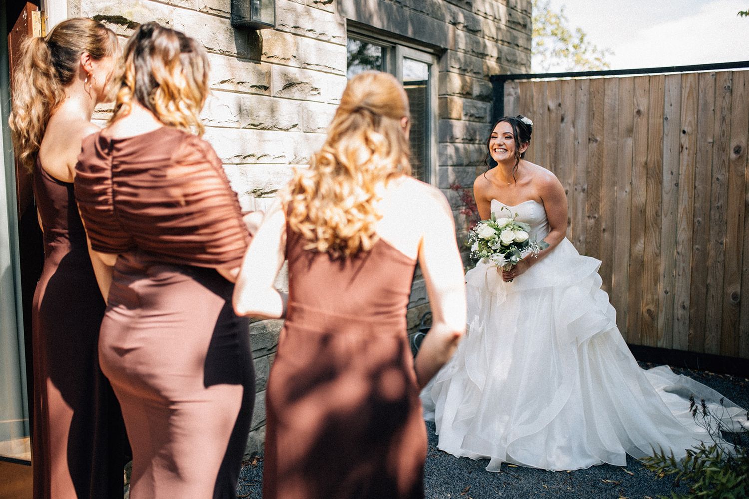 Smiling bridesmaid in a dark brown dress carries an orange and yellow bouquet down the aisle of a rustic barn wedding venue.