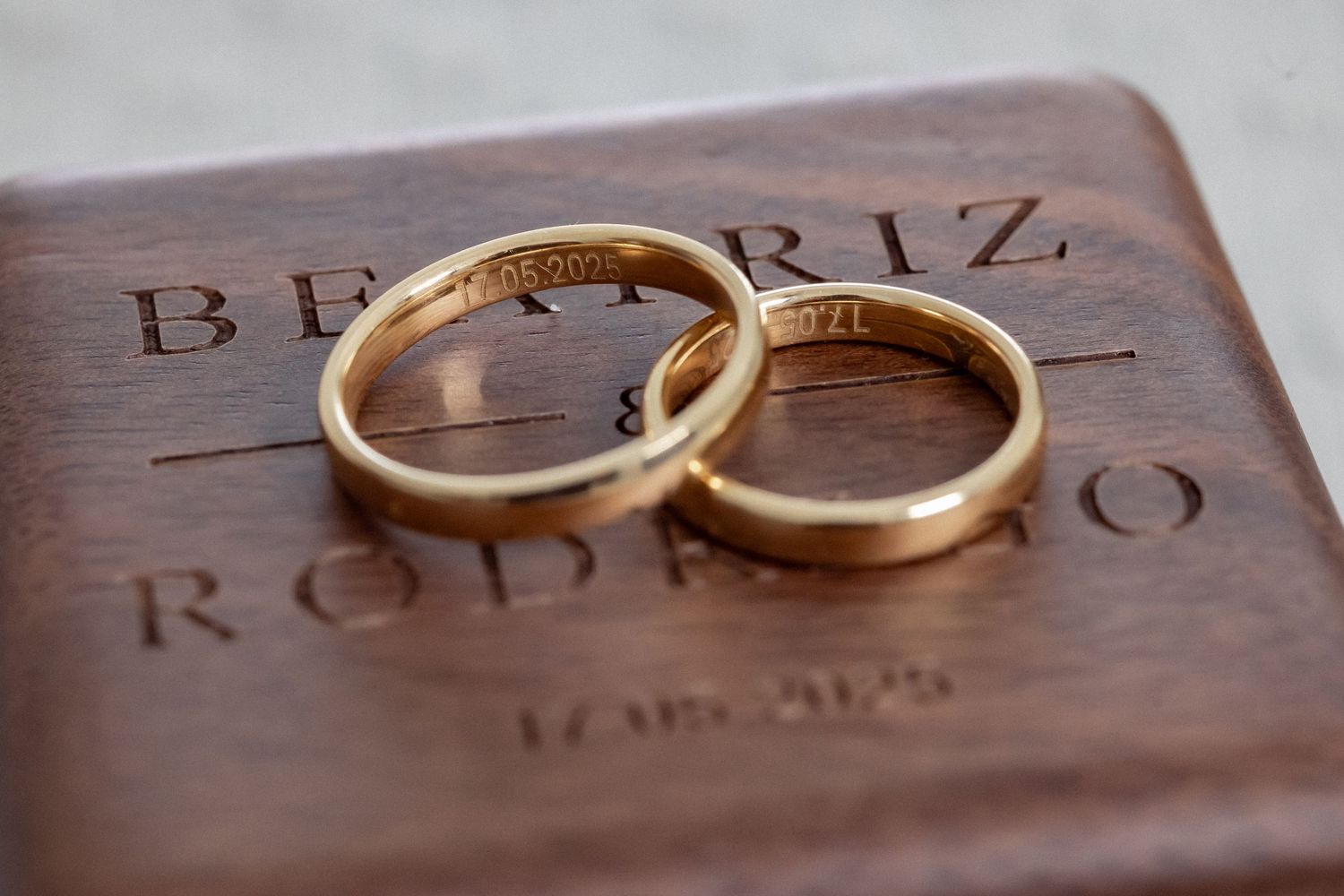 Two gold wedding bands resting on an engraved wooden ring box inscribed with Beatriz and Rodrigo.