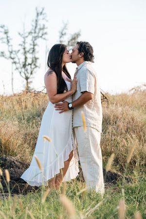 Couple kissing in a golden field at sunset, woman in white dress, man in beige linen outfit, romantic outdoor portrait.