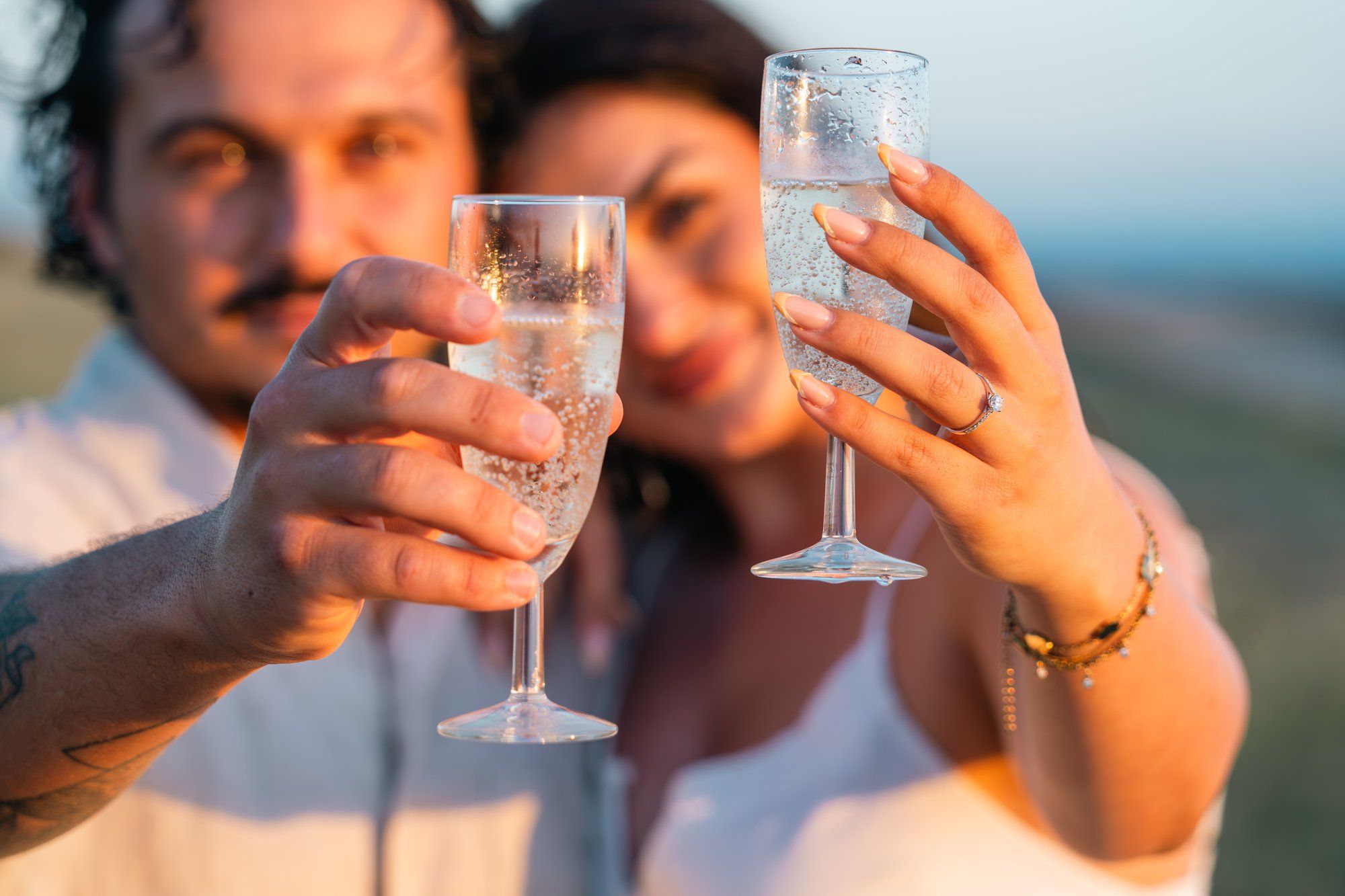 Couple clinking champagne glasses in a romantic outdoor toast, celebrating a special occasion together.