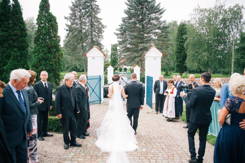 Brudepar går mellem gæster ved indgangen til en have – bryllupsfoto af Martin & Louise