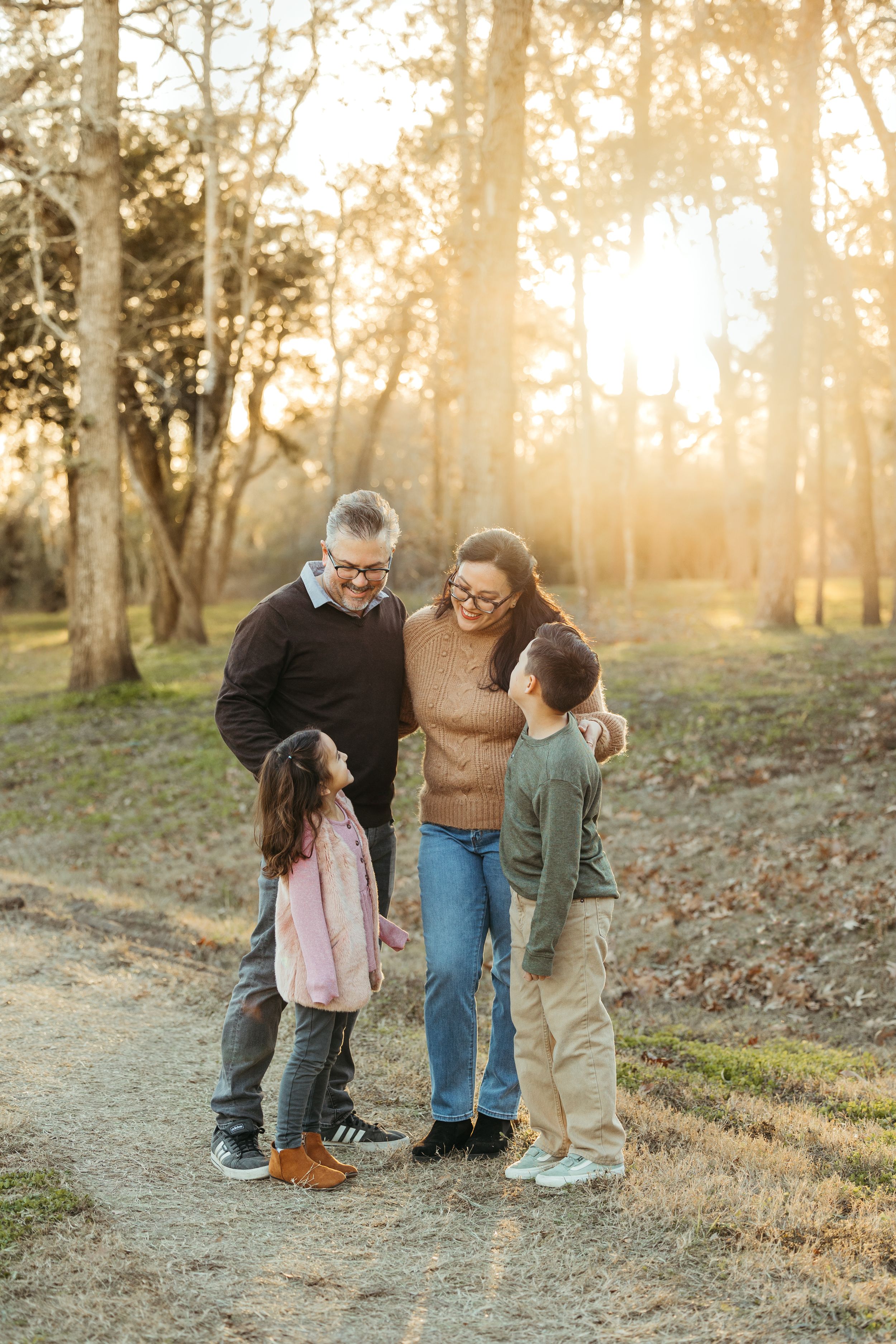 Family of four sharing a joyful moment on a sunlit forest path during golden hour.
