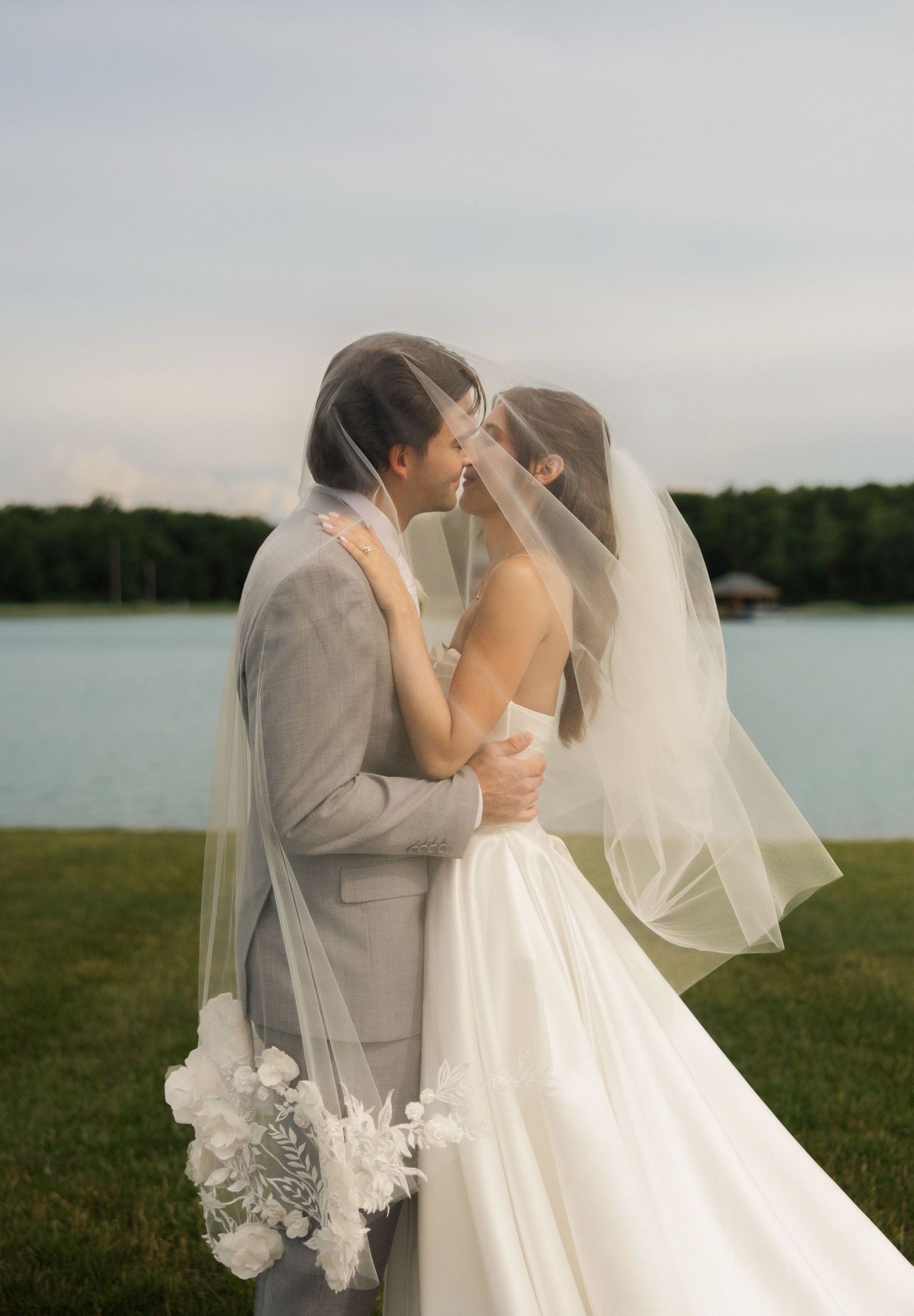 Bride and groom share a romantic kiss under a flowing veil outdoors near a lake at Tall Oaks Resort near Cleveland, Ohio