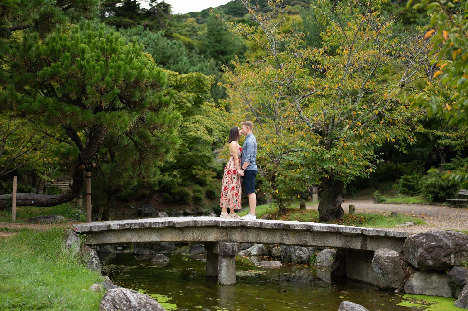 Couple standing together on a stone bridge over a tranquil pond in a lush Japanese garden.