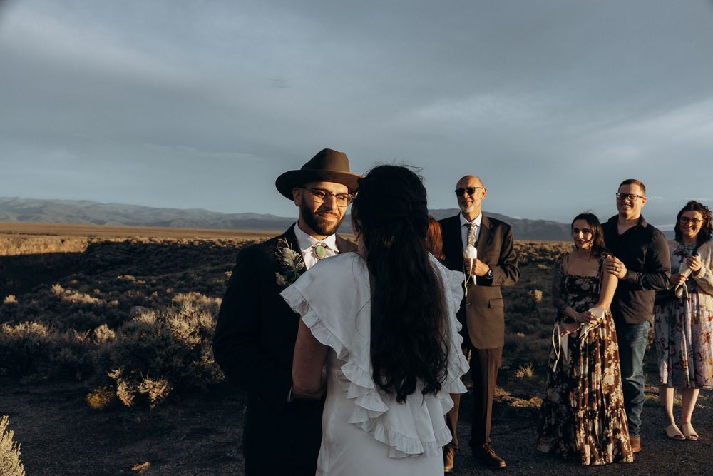 Couple exchanges vows at outdoor desert wedding ceremony with guests gathered under dramatic cloudy sky.