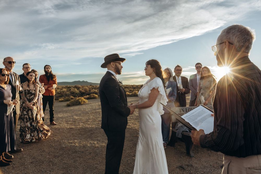 Outdoor desert wedding ceremony at sunset with couple exchanging vows before officiant and guests.
