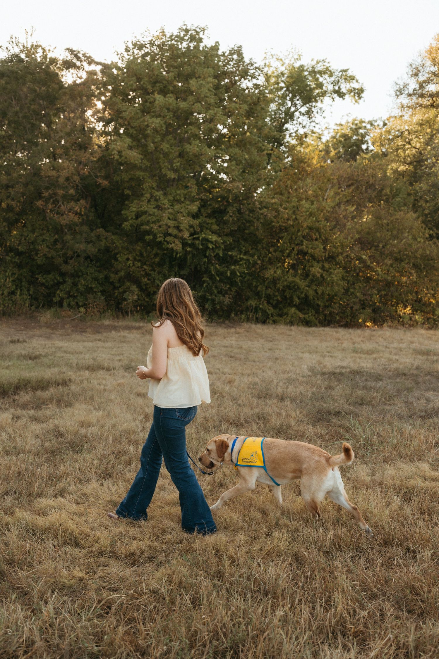 Senior girl walking through a field with her Canine Companion during senior photos at Oak Point Nature Preserve