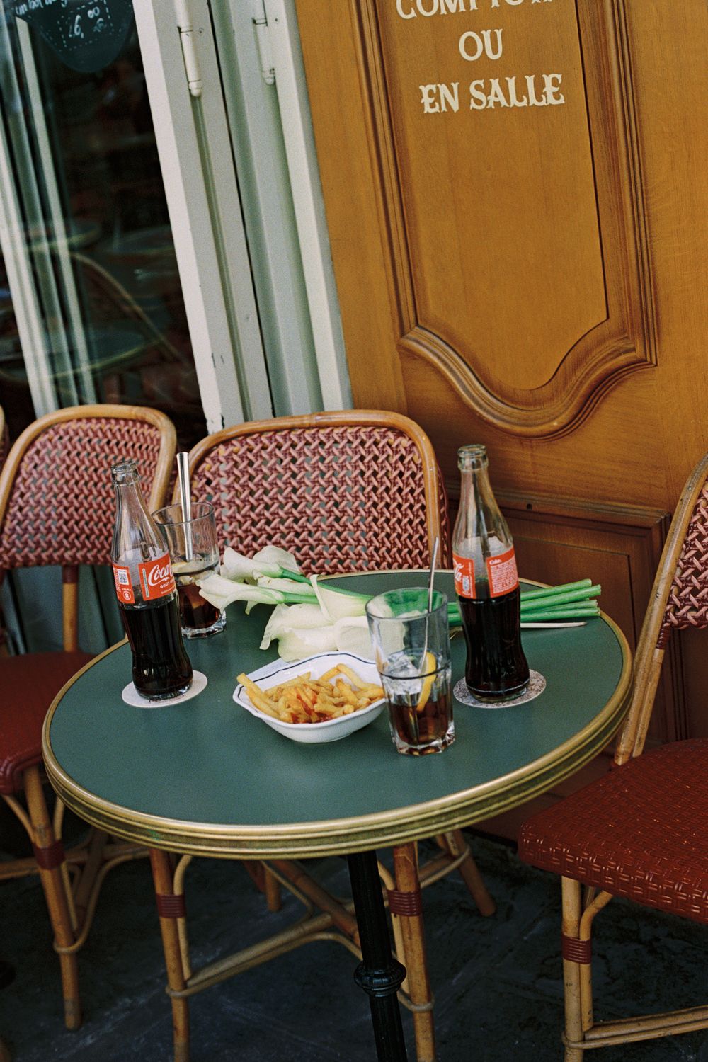 Parisian cafe terrace with green table, Coca-Cola bottles, snacks, and wicker chairs outside a French bistro. paris fiml photographer