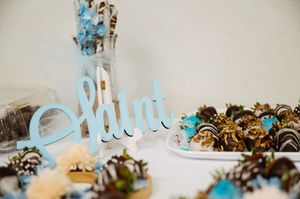 Mint-themed dessert table with chocolate-covered strawberries and blue decorative sign at a baby shower.