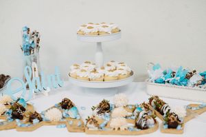 Elegant dessert table with tiered cupcakes, chocolate-dipped strawberries, and blue candy treats on a white background.