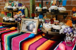 Colorful Mexican fiesta dessert table with cupcakes, maracas, and vibrant serape tablecloth for a festive celebration.