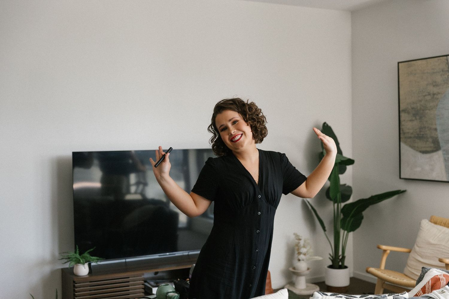 Happy bride in black dress dancing joyfully in a modern living room before wedding.