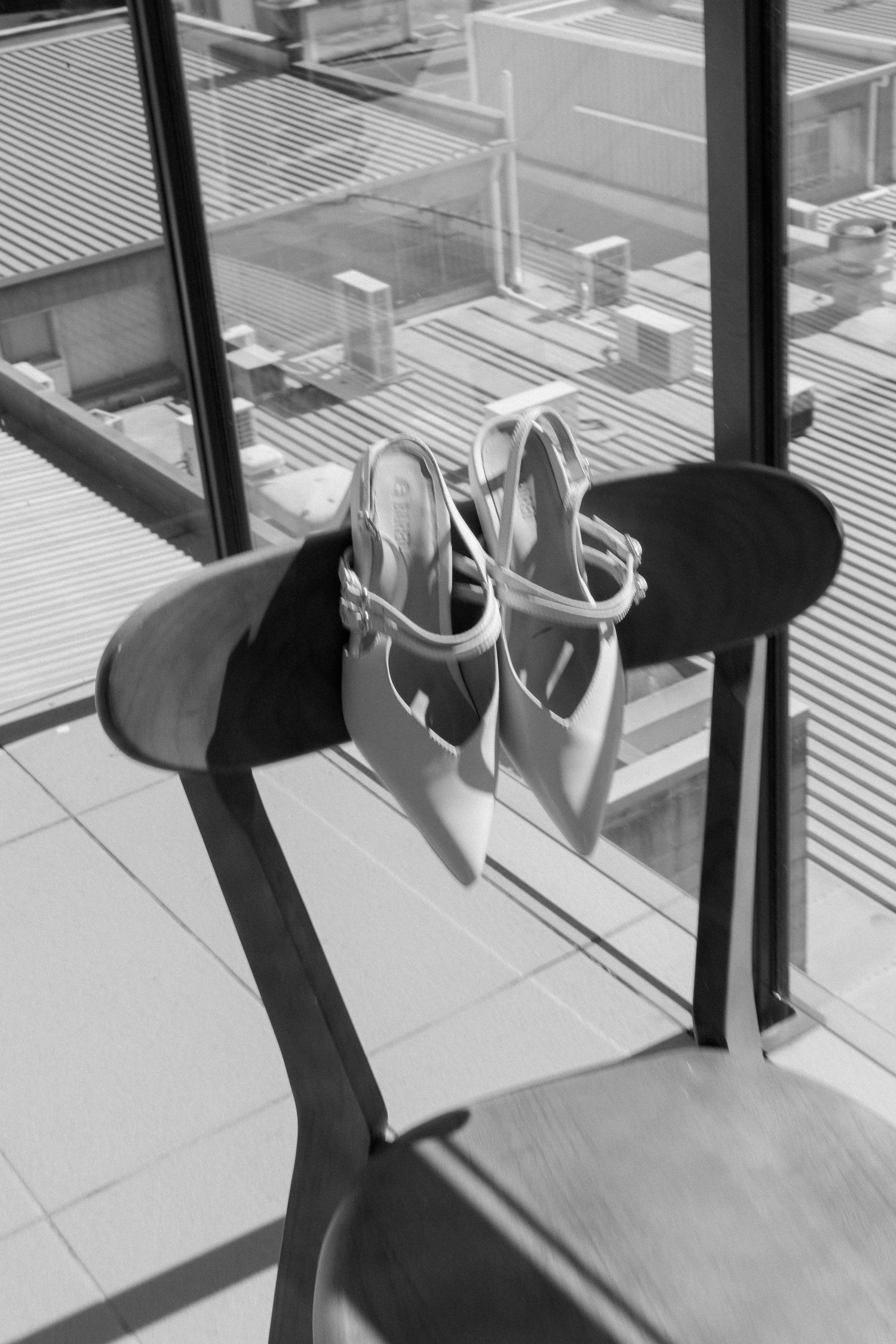 White bridal heels resting on a chair near a window with city views below.