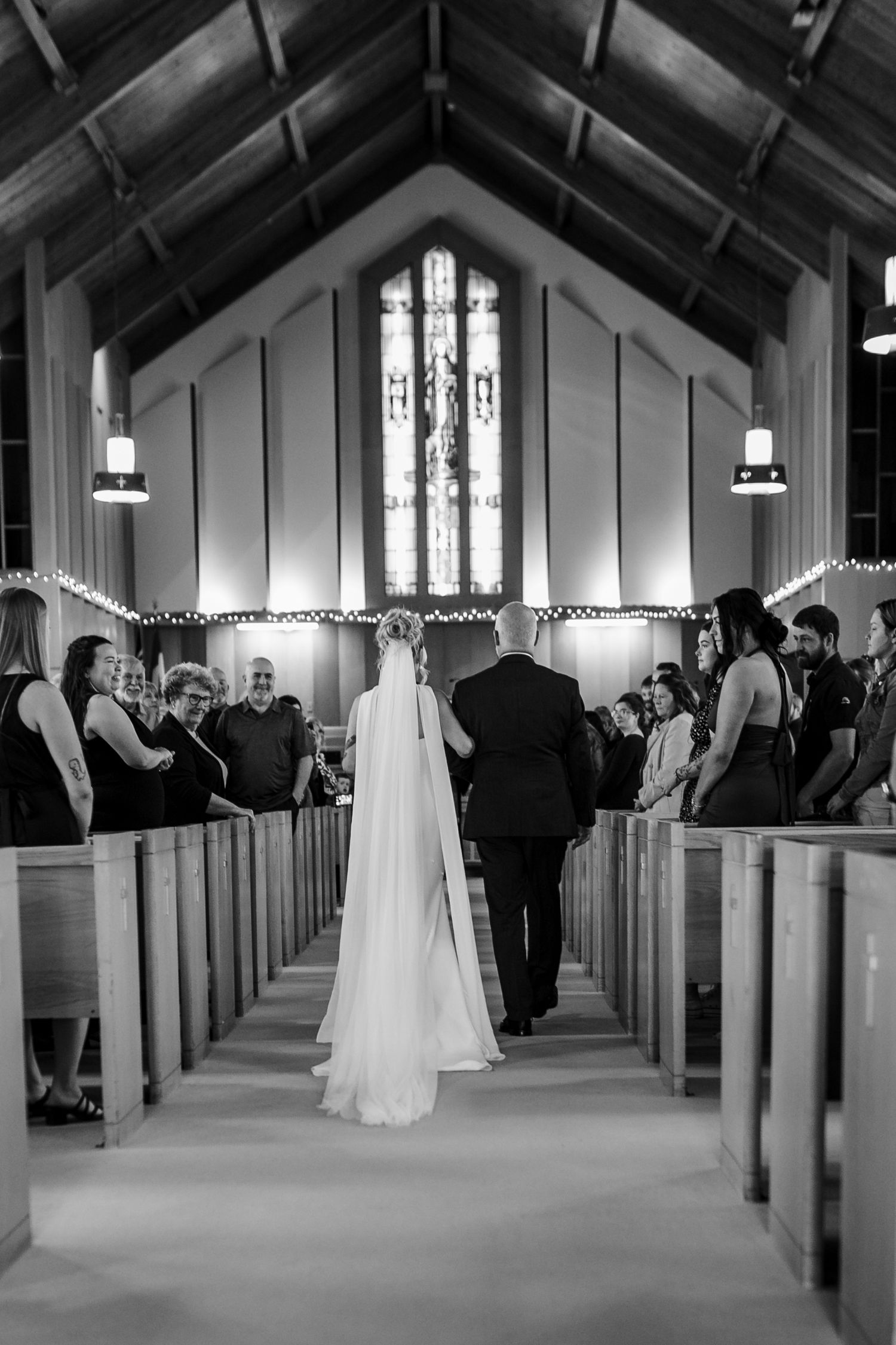 Black and white photo of a bride walking down the church aisle with her father during a wedding ceremony.