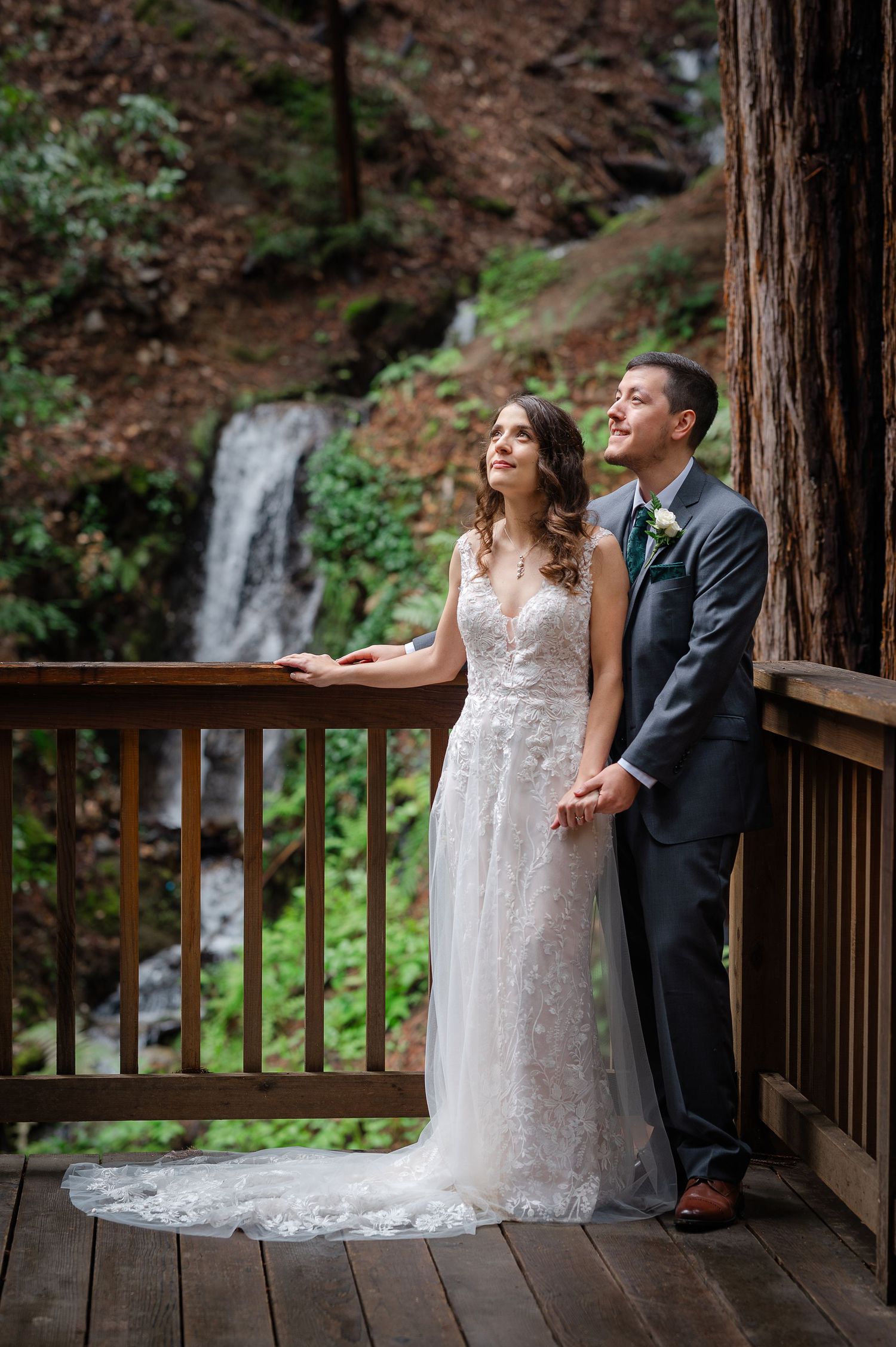Rustic outdoor wedding venue with ornate iron gates opening to a forest dining setup with string lights and redwood trees.