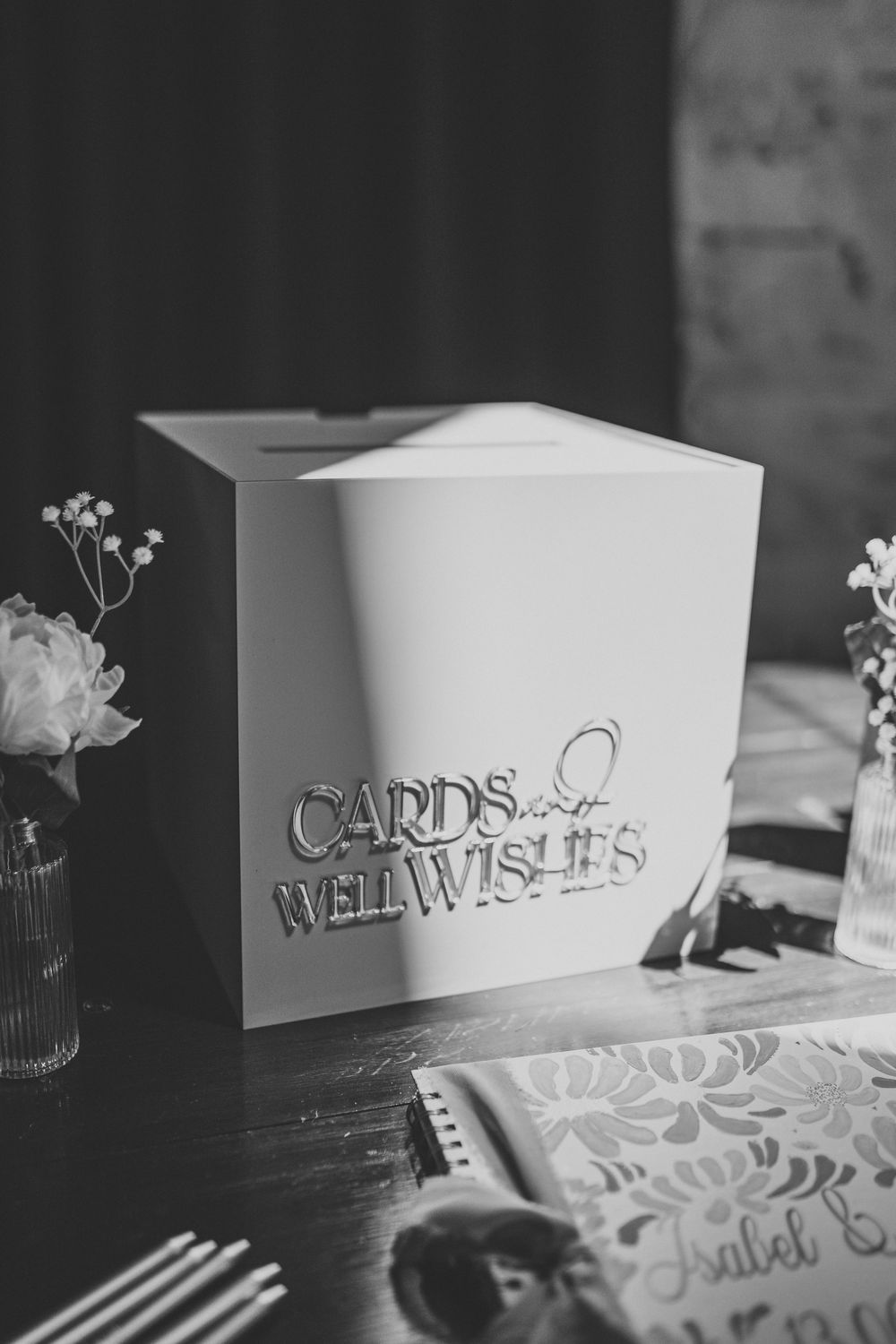 Black and white photo of a white wedding card box labeled Cards and Well Wishes on a decorated table.